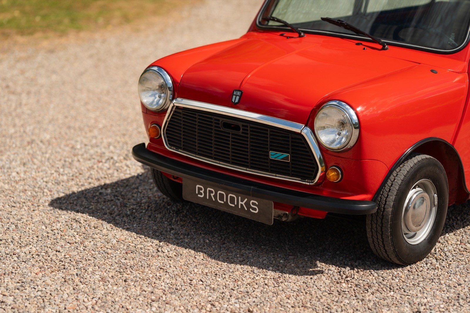Close-up of a bright red car parked on a gravel surface, focusing on the front grille and headlights.