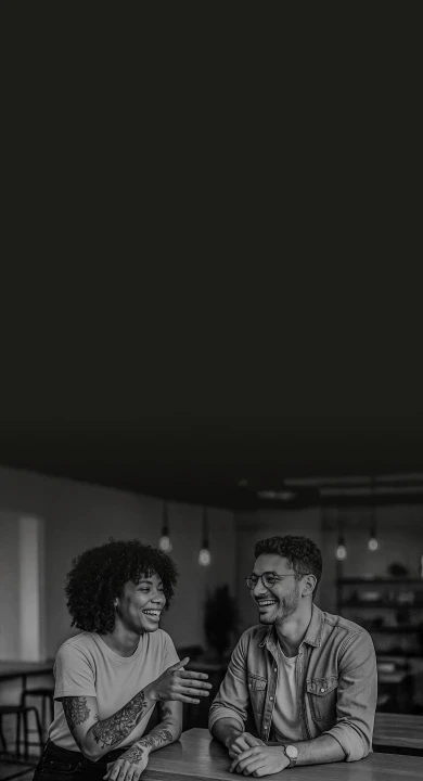 Casal de empreendedores em ambiente moderno e acolhedor, sorrindo em momento de colaboração.