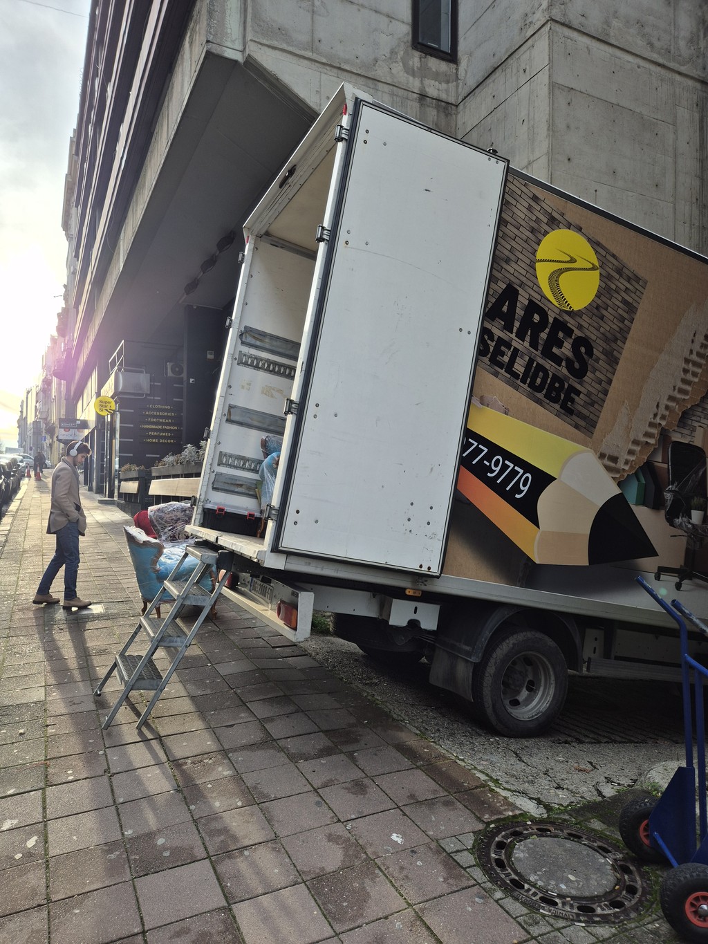 Kamion za selidbe na trotoaru sa metalnim stepenicama i otvorenim teretnim prostorom.