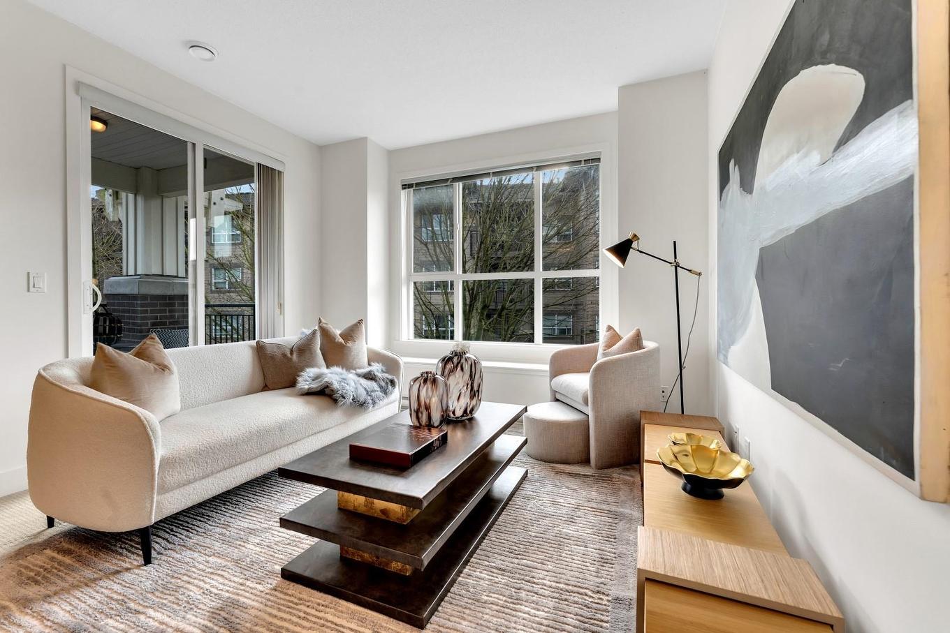 A modern living room featuring a light sofa, wooden furniture, and large windows letting in natural light.