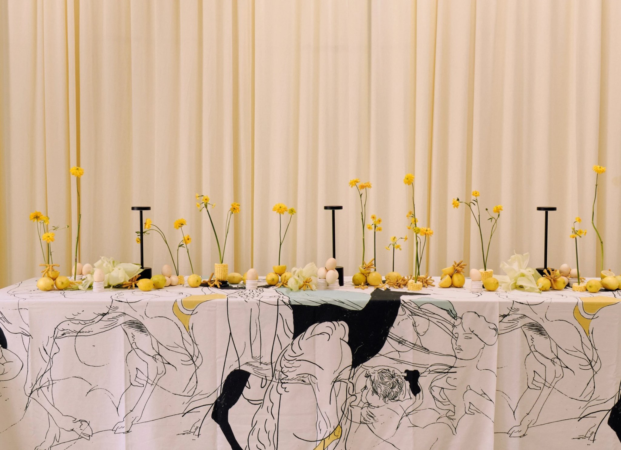 Mesa decorada con limones, flores amarillas y textiles ilustrados.