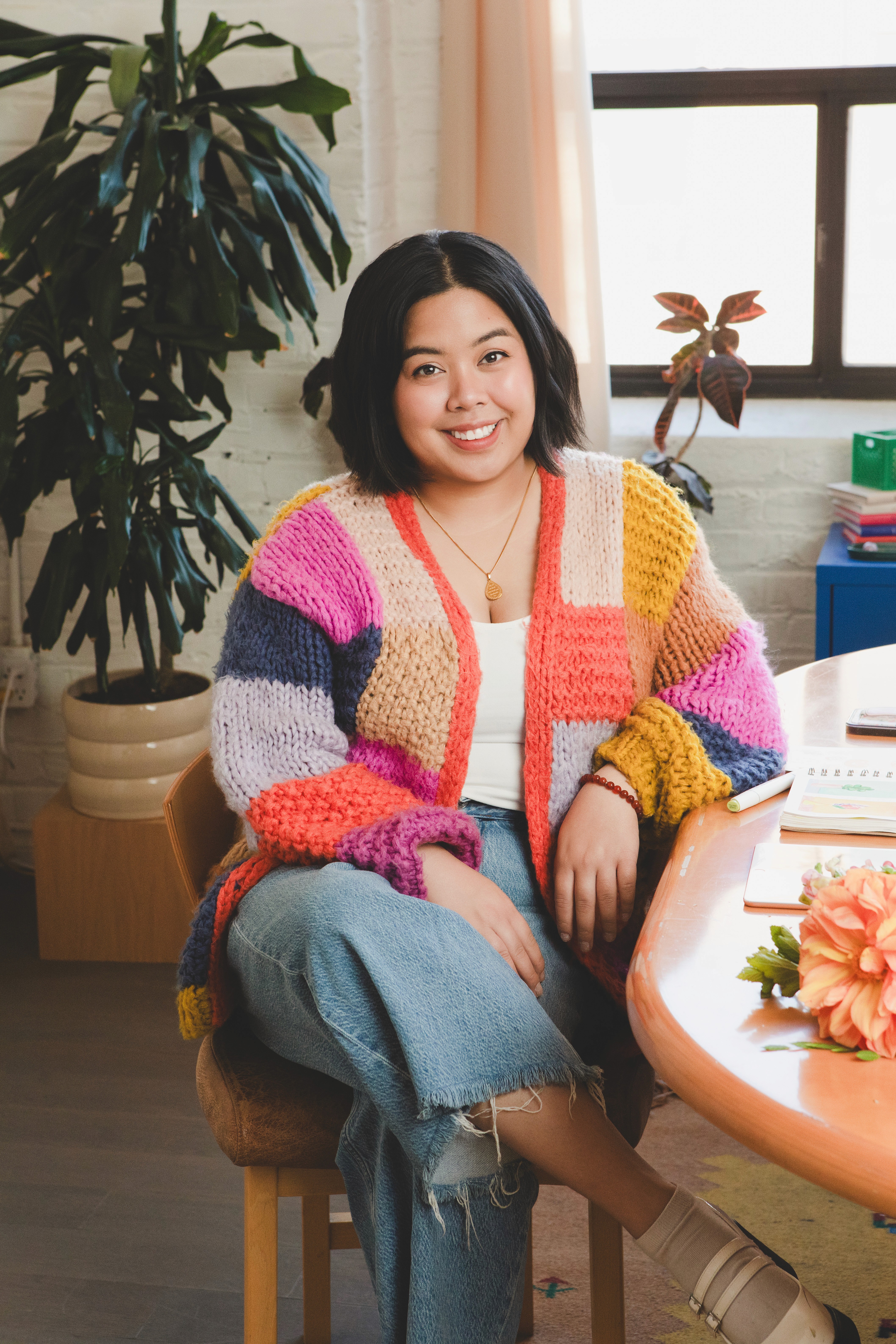 designer wearing colourful cardigan sitting crossed-legged at desk