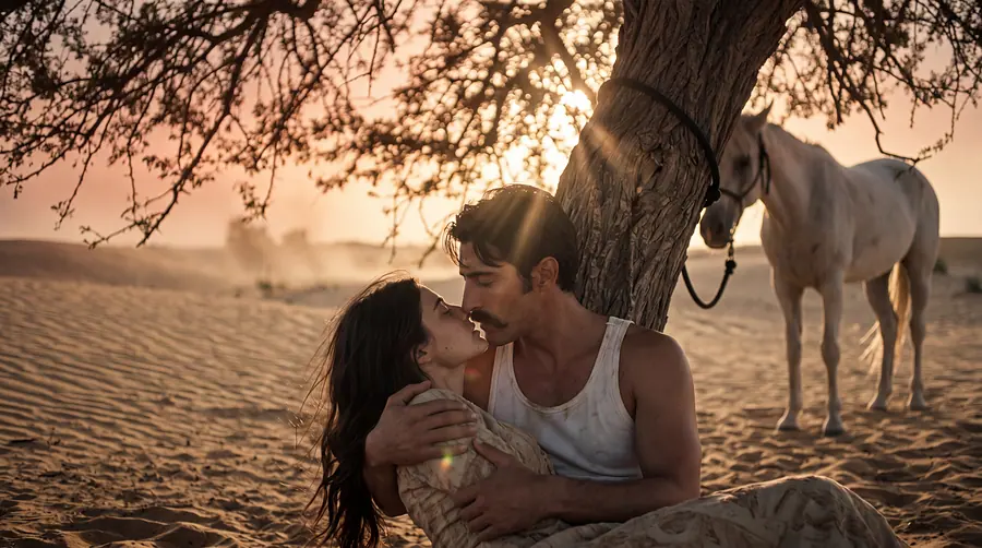 Two people embracing under a desert tree at sunset, a white horse behind