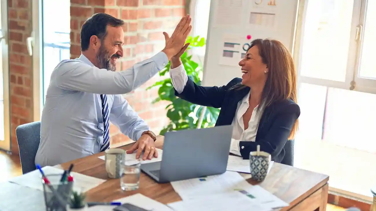 Two business professionals celebrating with a high five during a meeting, illustrating sponsorship as a clear business case, tax-deductible marketing spend and a successful sports sponsorship partnership.