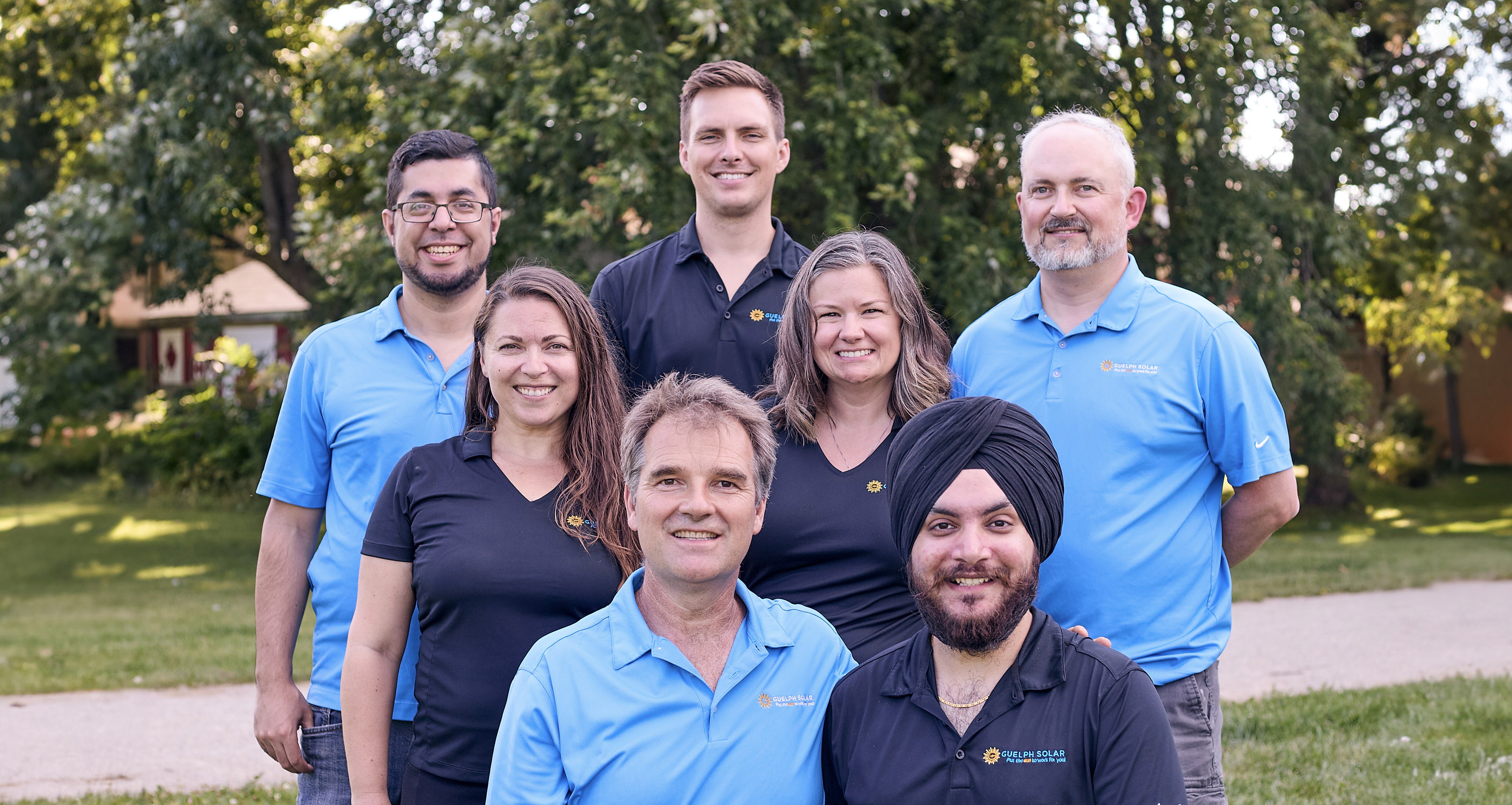 The Guelph Solar team, wearing matching blue shirts, posed together outdoors with trees in the background.