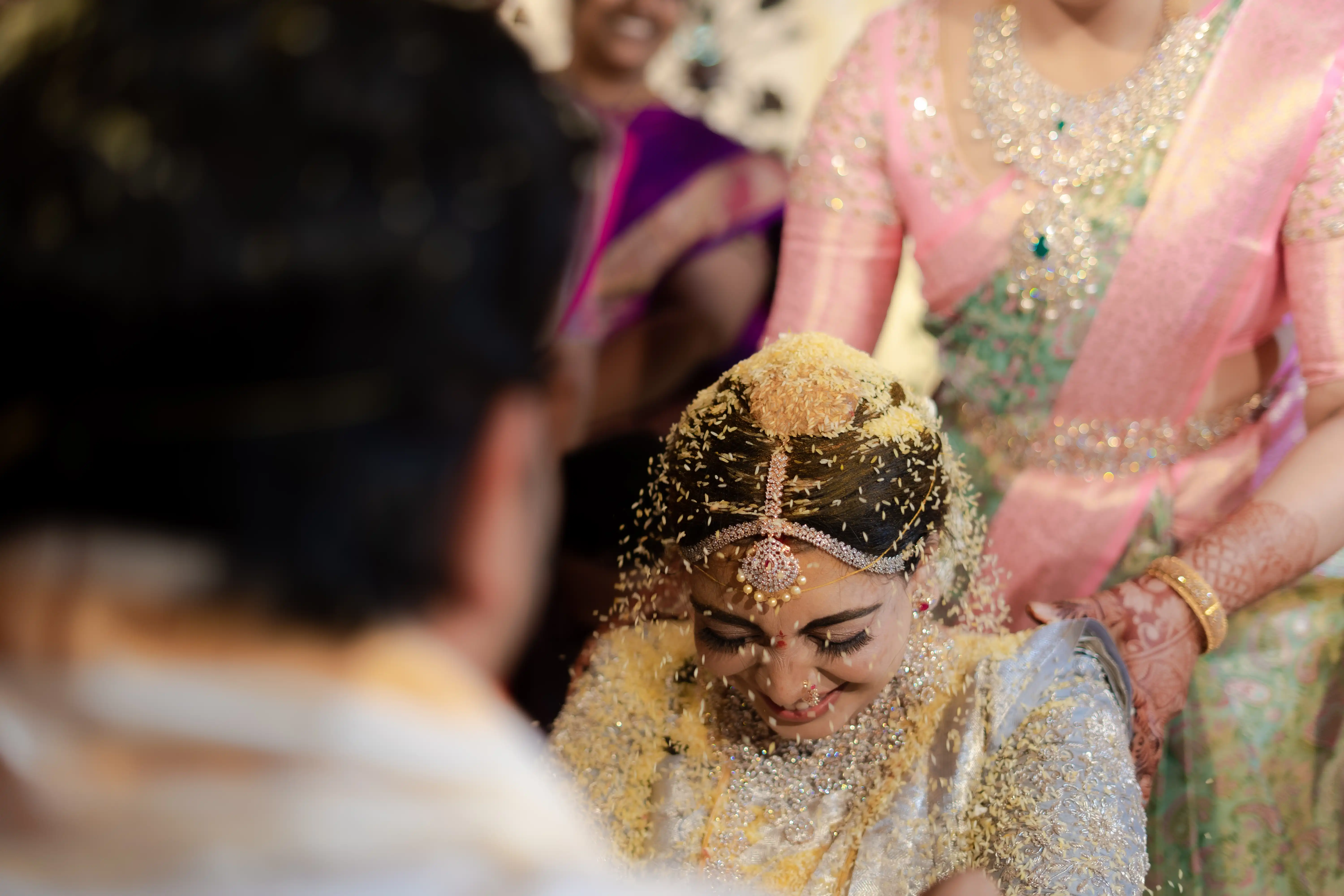 Priya, the bride, being showered with rice during a festive ceremony with loved ones. Fine Art Wedding Photography in Hyderabad by Out of The Blues.