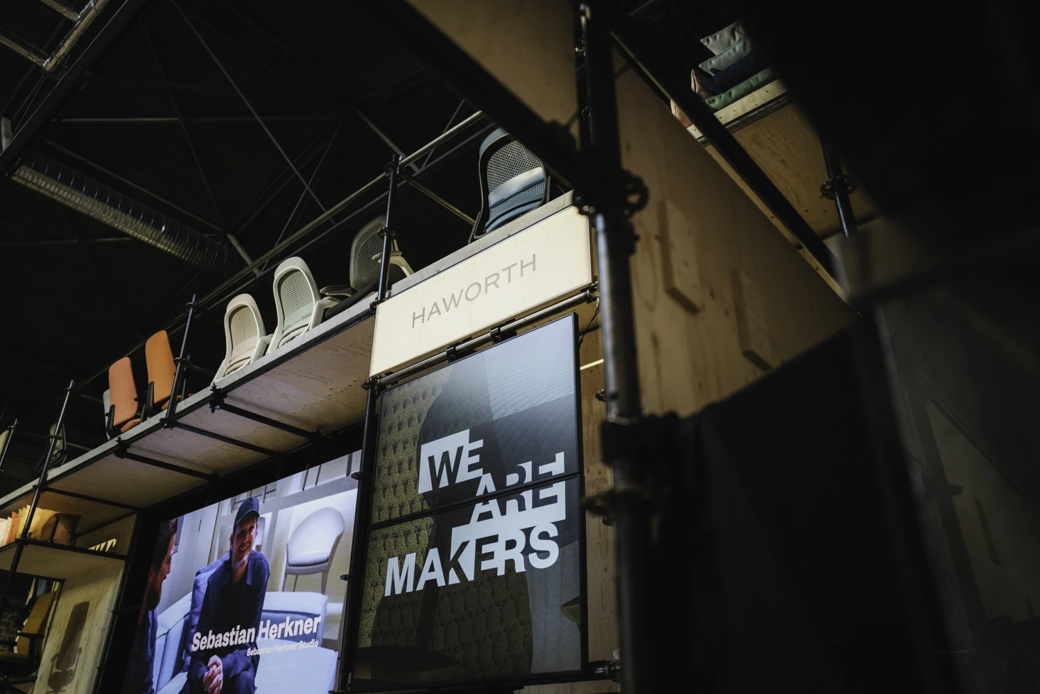 Haworth sign and We Are Makers screen on the scaffold booth with chairs lined up above.
