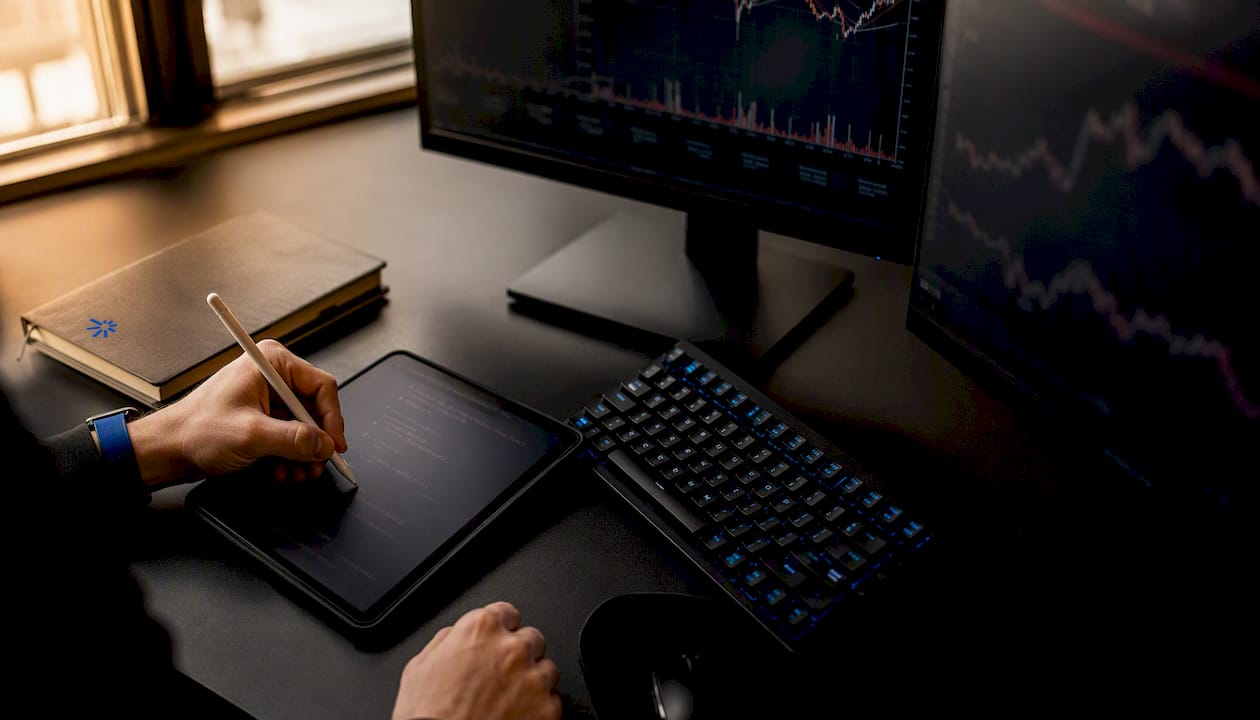 Close-up of hand with stylus near screens showing trading graphs