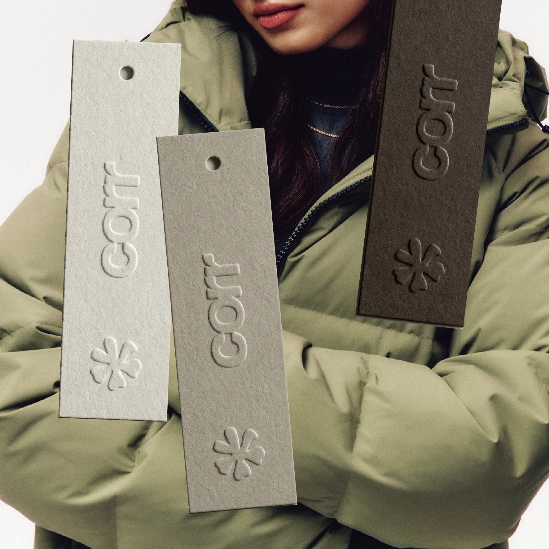 A women wearing a coat with 3 overlaid hang tags with a corr wordmark logo and a snowflake motif embossed on them