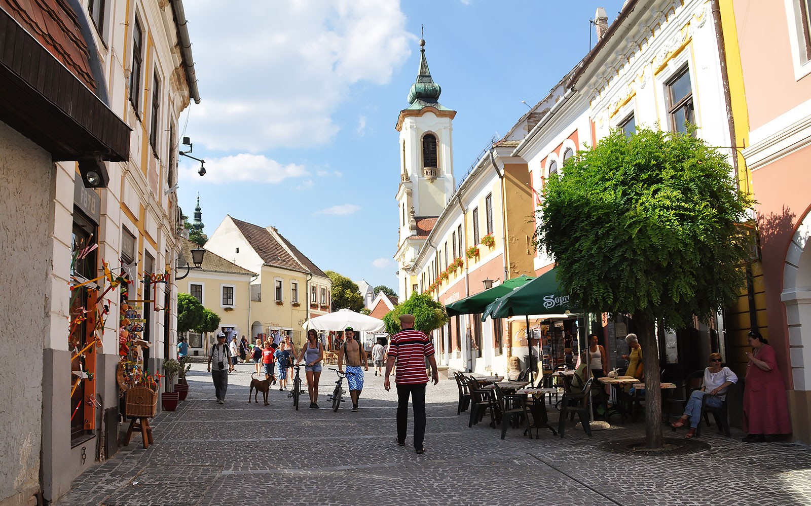 Street scene in Szentendre with people walking and a church tower in the background.