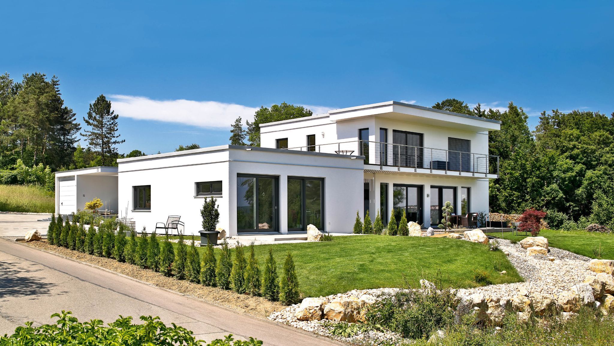 Moderne weiße Villa mit Balkonen, großen Fenstern und einem gepflegten Garten bei Sonnenschein.