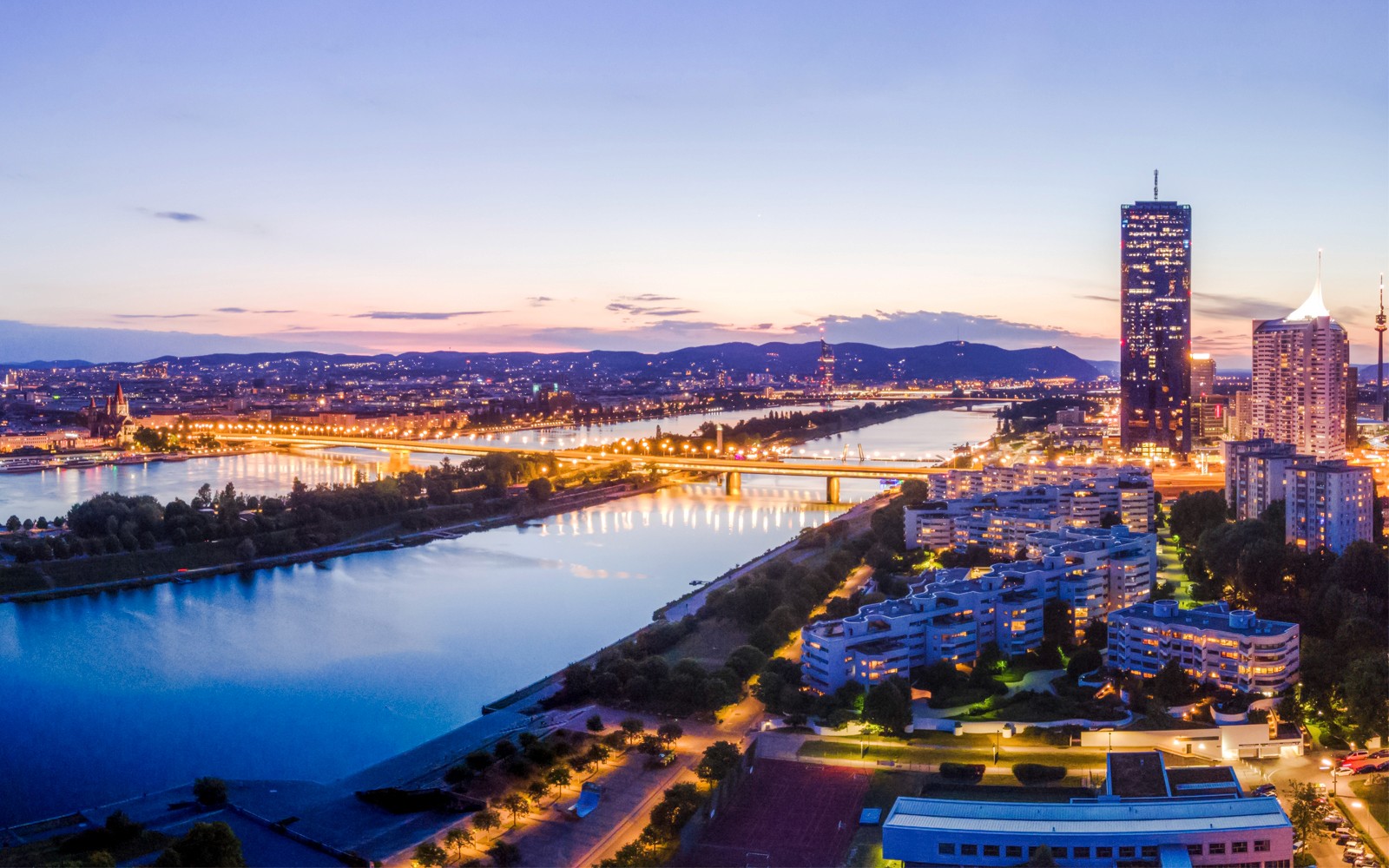 Ilmakuva Wienistä hämärässä, jossa valaistu kaupunkimaisema ja Tonava.