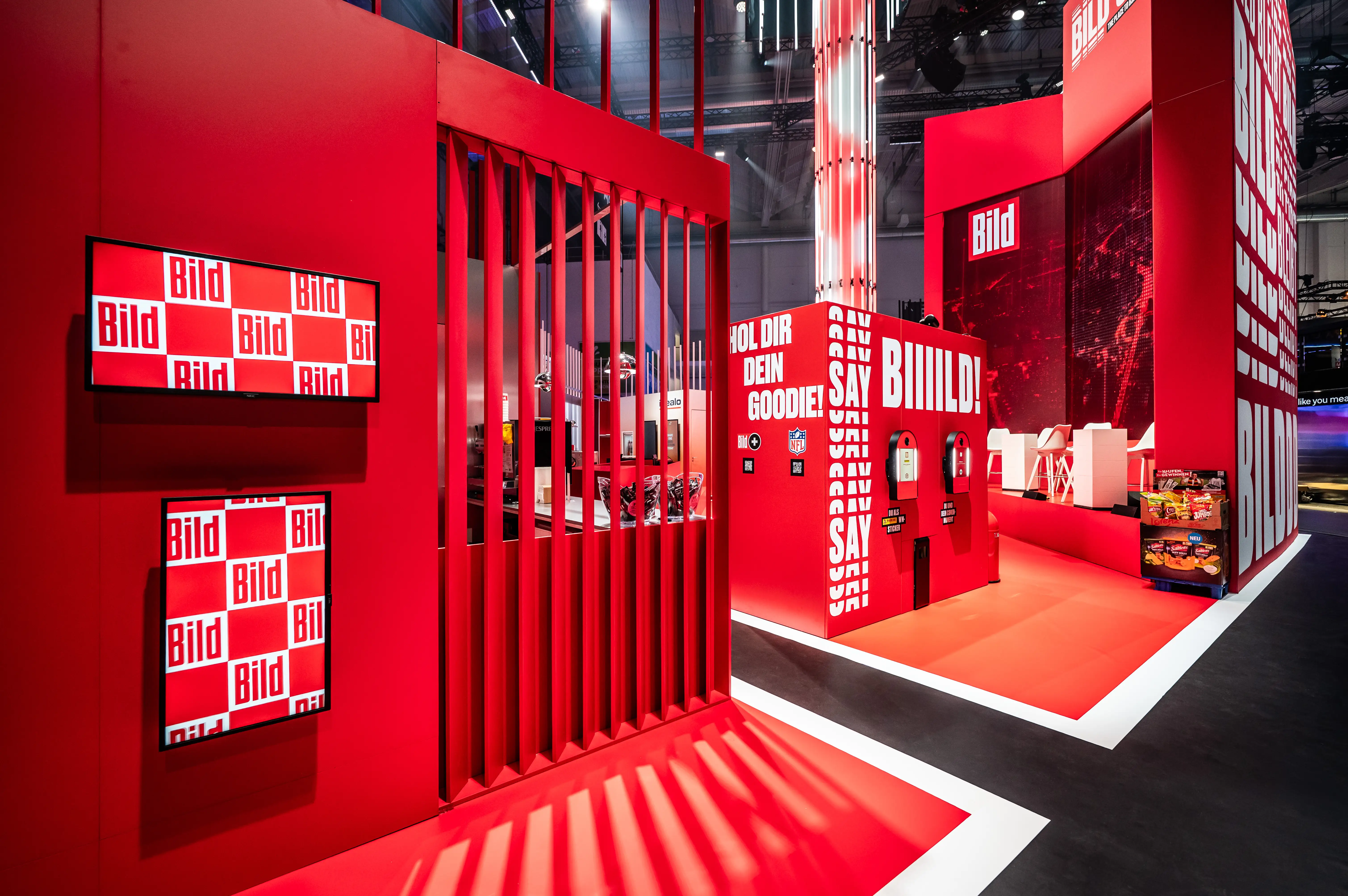 Red goodie area at the Bild OMR booth with checkerboard logo screens, slatted wall and dispenser stations.
