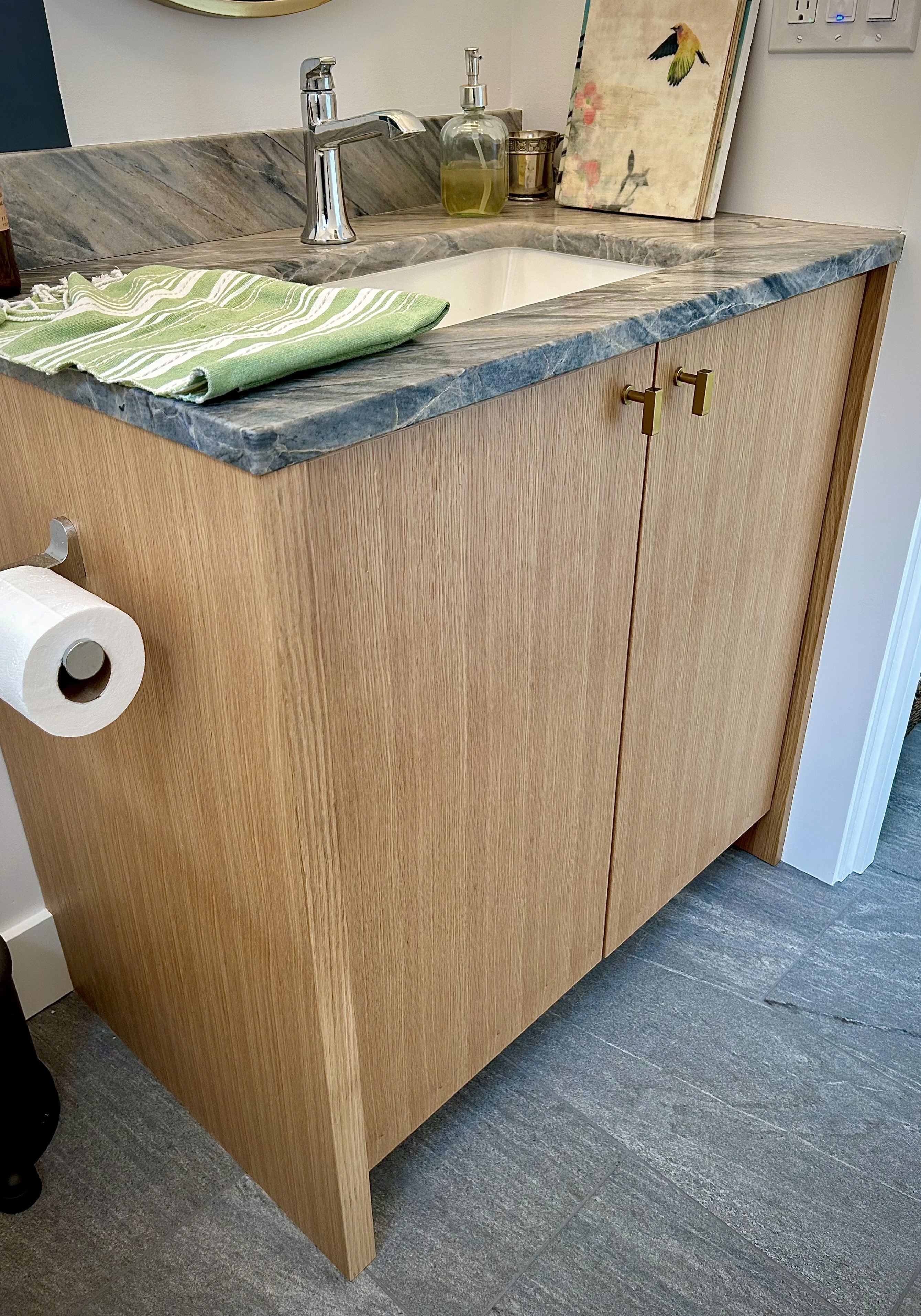 A white oak powder room vanity with green stone countertop and undercounter sink.