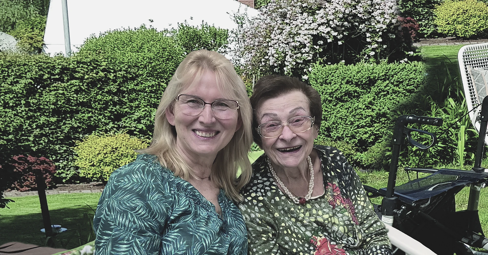 Zwei Frauen lächeln gemeinsam in einem Garten.