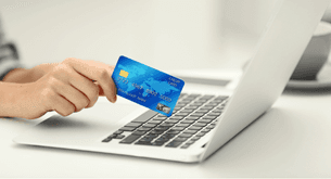 A person holds a credit card over a laptop computer.