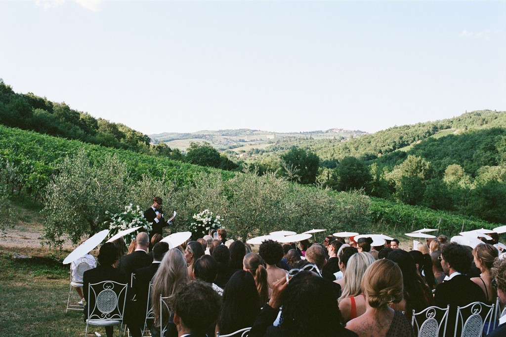 Guests seated with paper umbrellas during an outdoor wedding ceremony in a vineyard setting