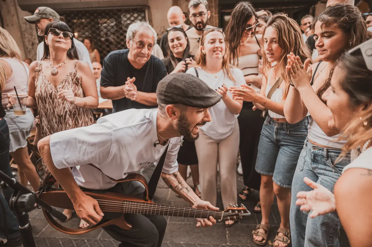 צילום רגע מלא אנרגיה ממופע רחוב של רני כהן. האמן נראה מנגן בגיטרה ושר בהתלהבות במרכז מעגל של קהל מוחא כפיים ומחייך באווירה חמה ואותנטית, מאת Shiriz Photography הצלמת שירי עציץ.