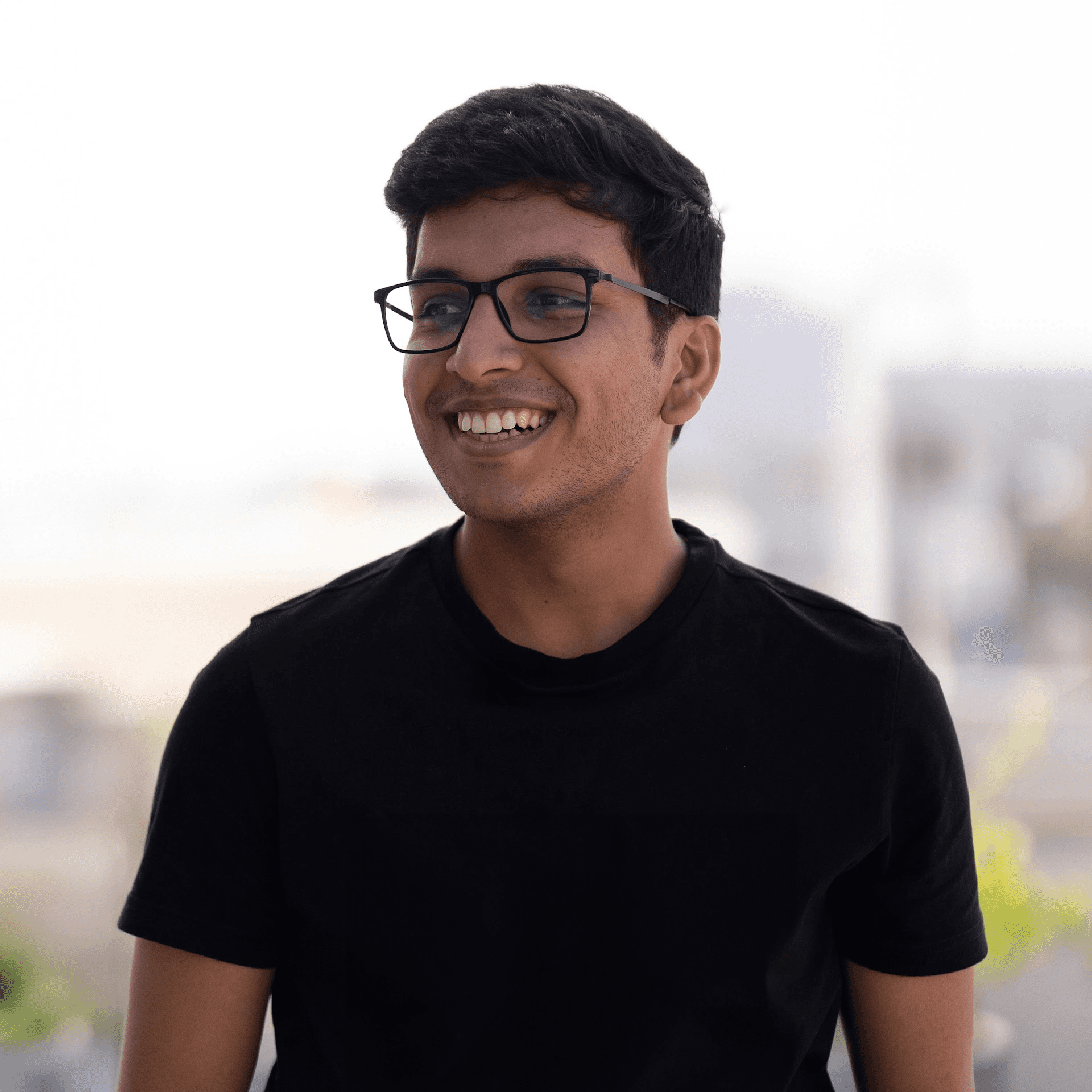 Smiling man with glasses and a short beard wearing a white t-shirt stands against a deep purple background, conveying a cheerful and friendly tone.