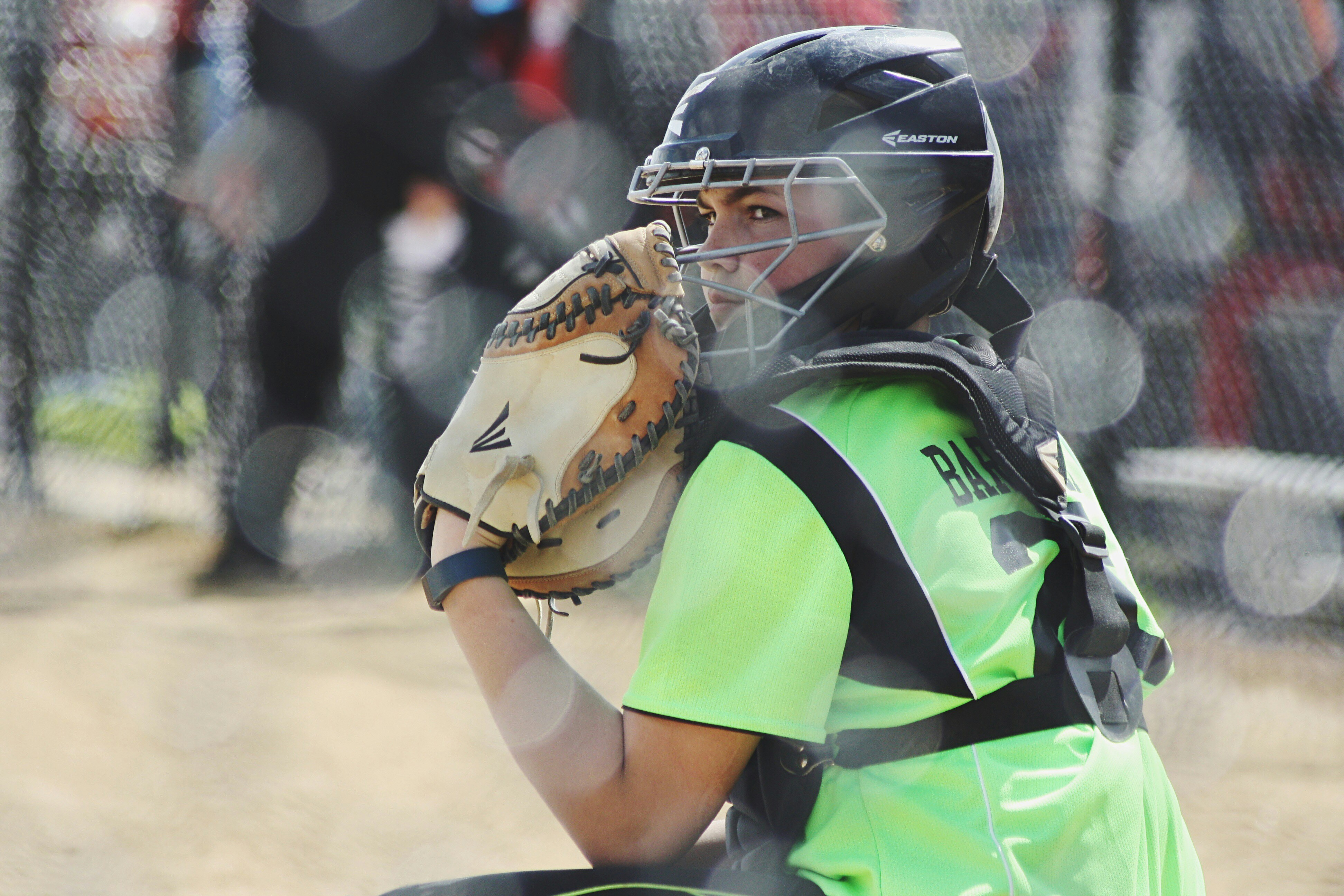 A softball catcher crouching, looking at the left with a glove close to her mask.