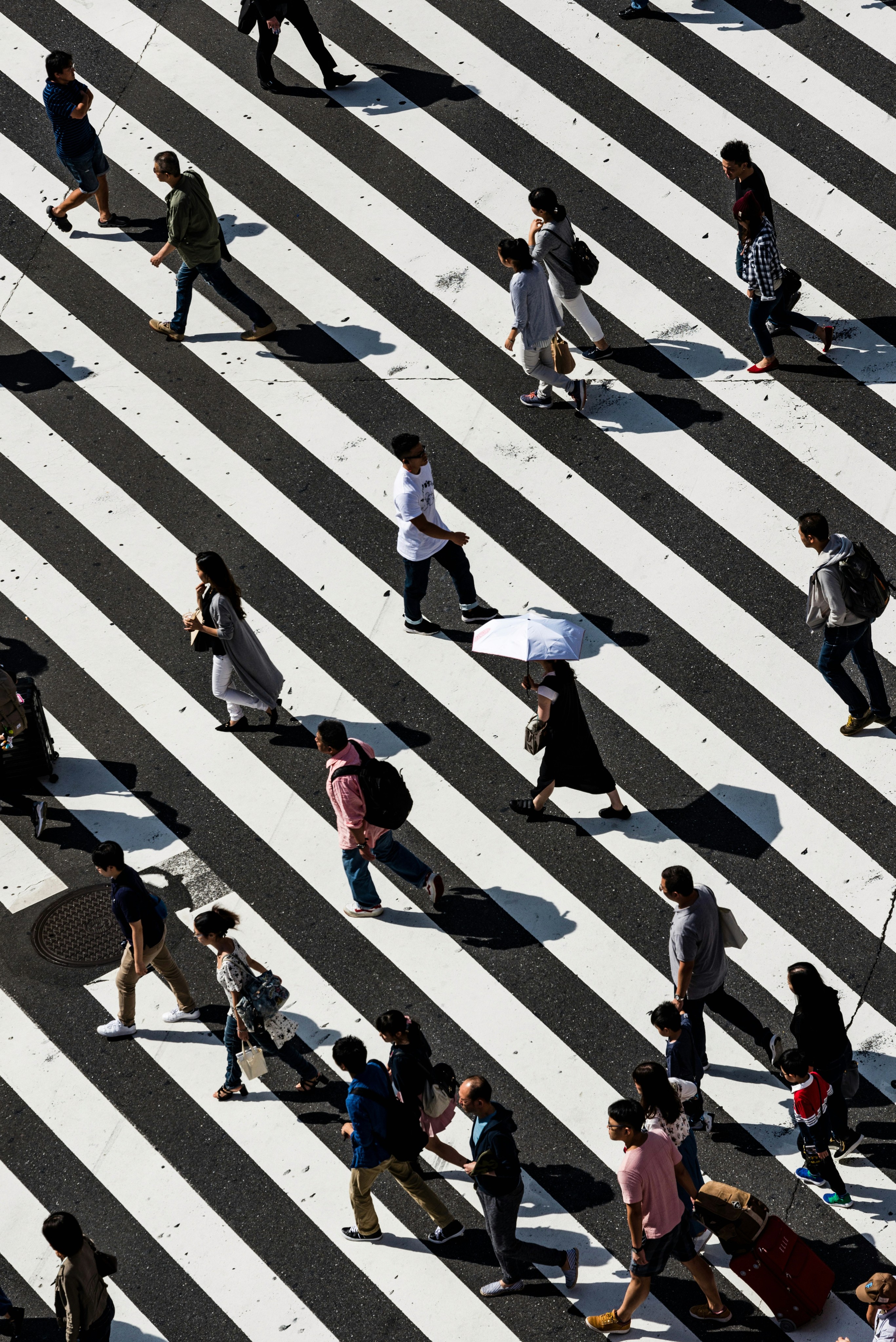 An overhead view of multiple people walking across a wide zebra crossing.