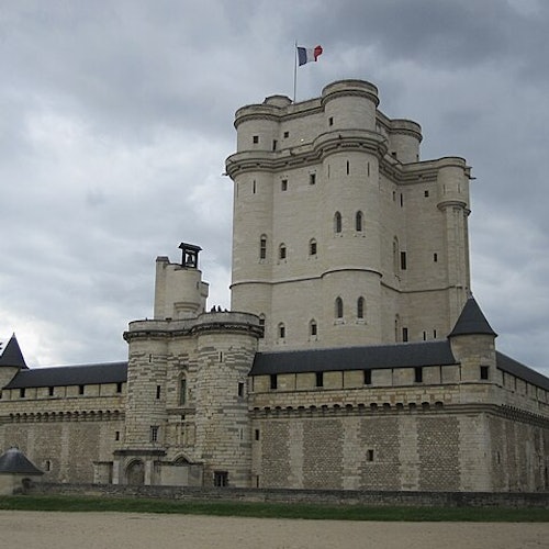 一座大型石头城堡,中央塔楼飘扬着法国国旗,天空阴云密布。