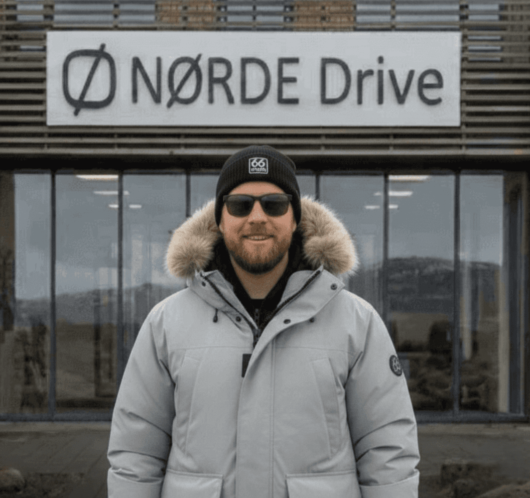 Man in a white parka standing in front of a modern building.