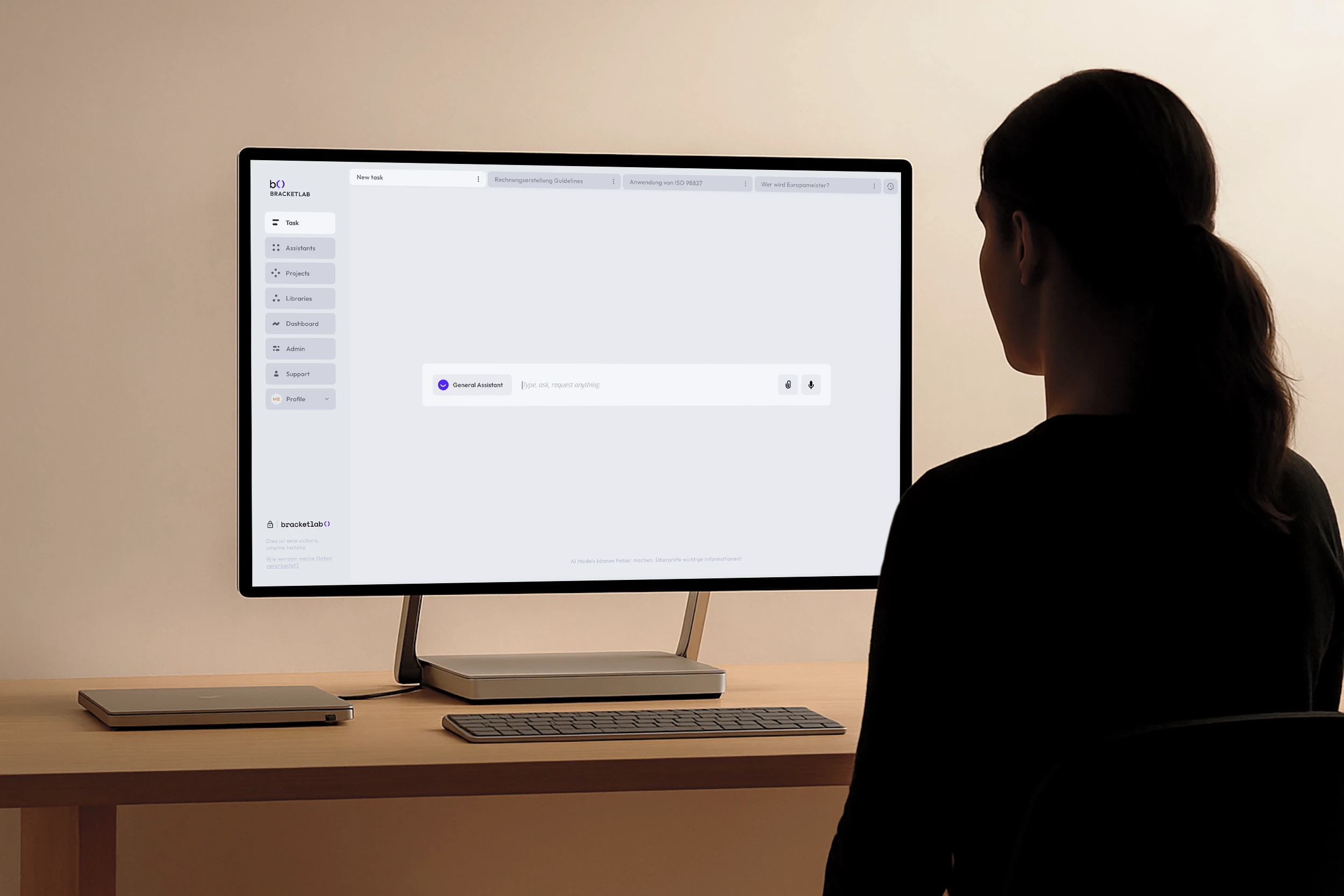 Woman in glasses and business-casual attire smiling confidently while standing in an office space with a corkboard in the background.