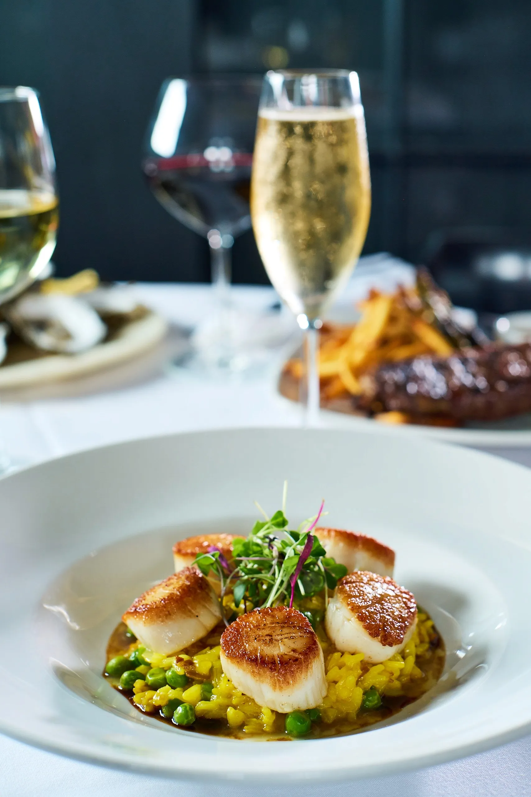 Seared scallops served over green pea risotto with microgreens on a white plate.