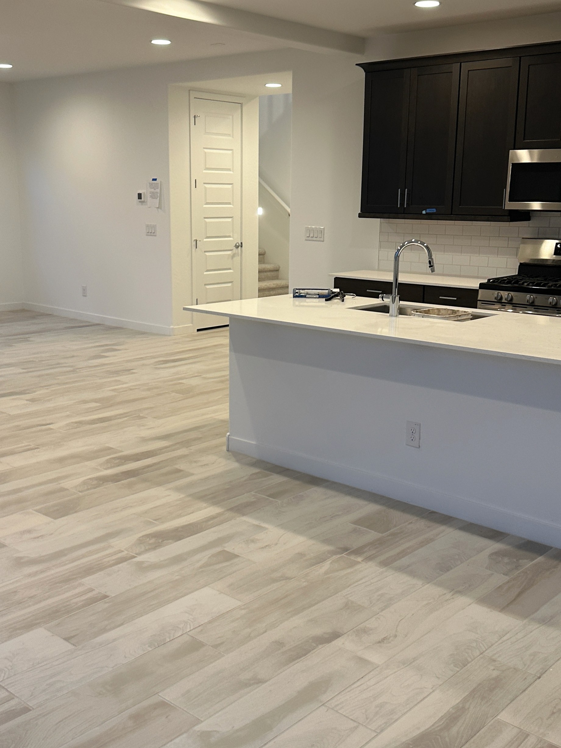 Modern kitchen with dark cabinets, white island, and wood-look tiles in an open-plan living area under construction.