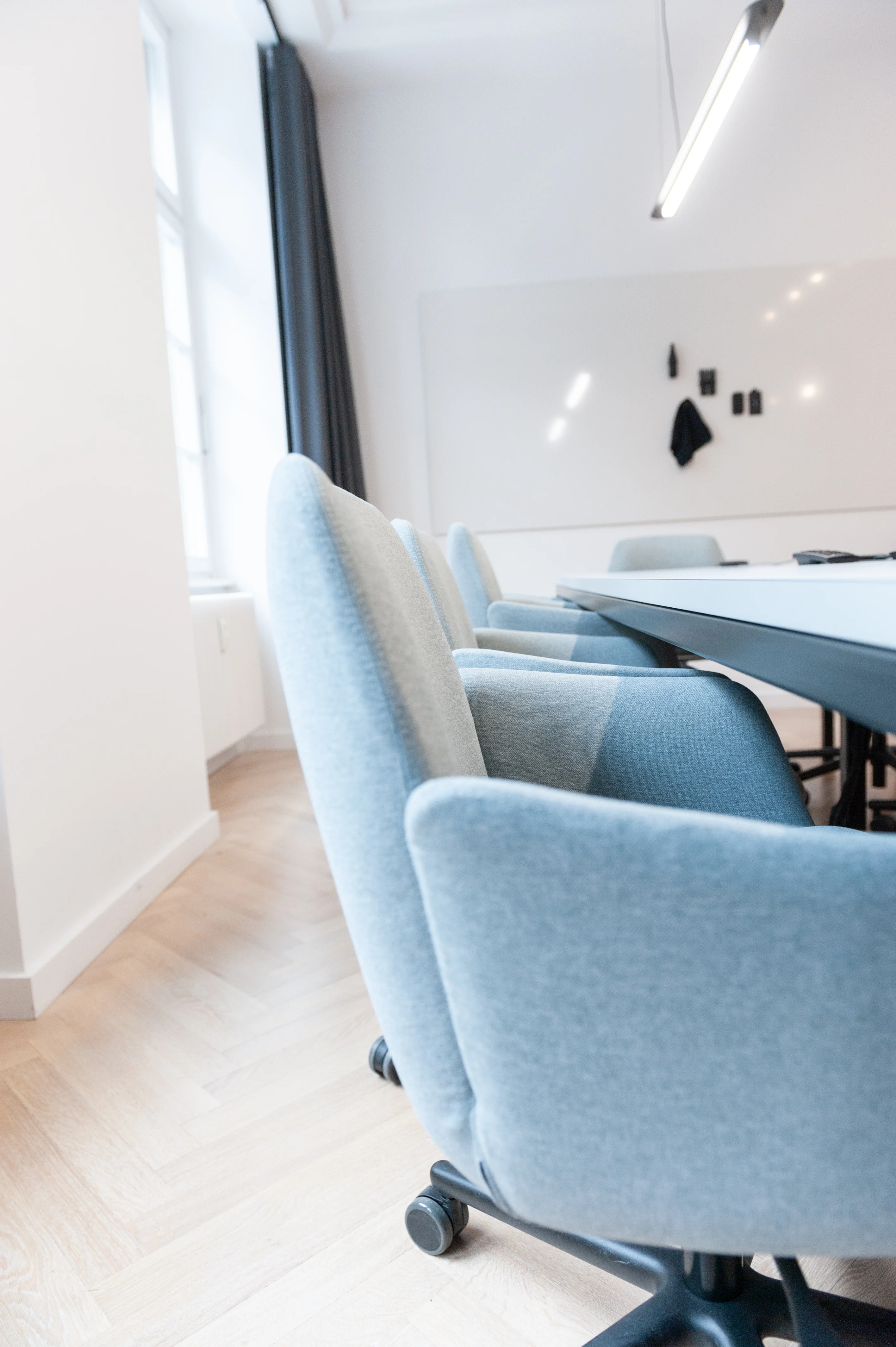 Close-up of pale blue upholstered swivel chairs with two-tone backs at a dark conference table at AI START-UP BERLIN, with a whiteboard and dark curtain behind.