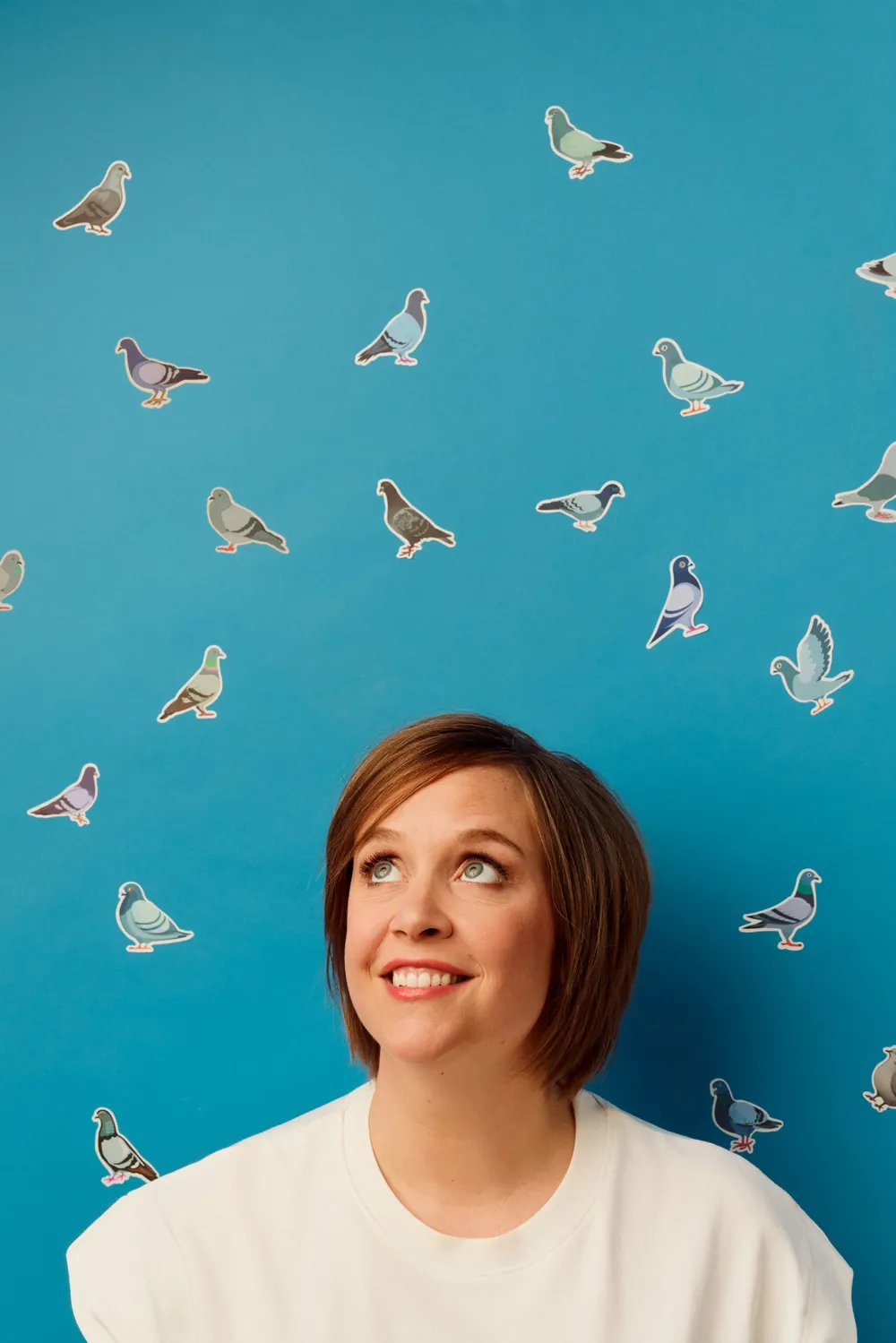 Portrait de Manon Lepomme souriante, regard levé vers des stickers pigeons sur fond bleu