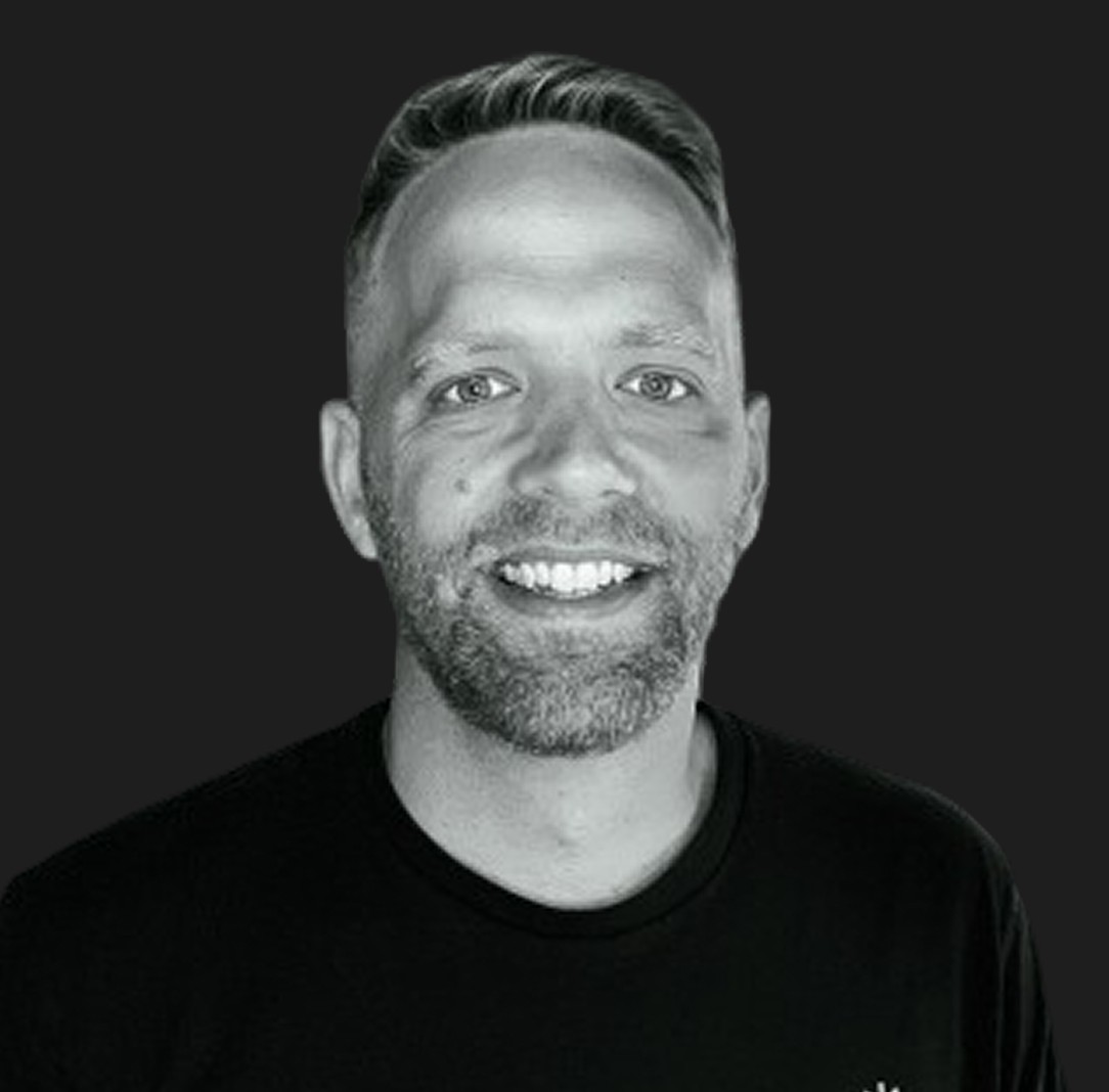 Black-and-white portrait of Ashley Swanson, the founder of Pixel Eye Studio, smiling with short hair, wearing a black shirt against a dark background.