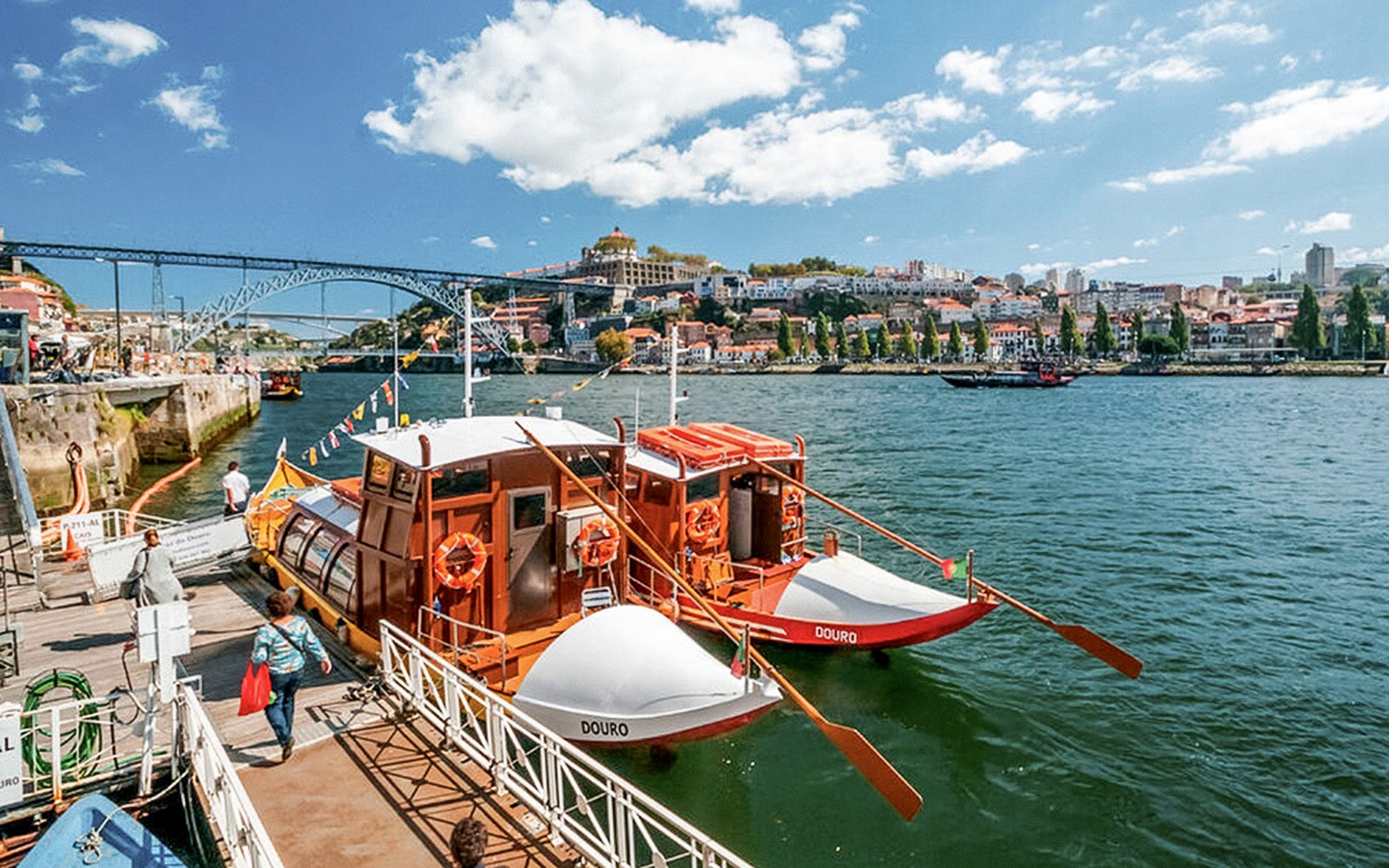 Turistas abordando un barco para un crucero por el río Duero en Oporto, con el puente Dom Luís I al fondo.