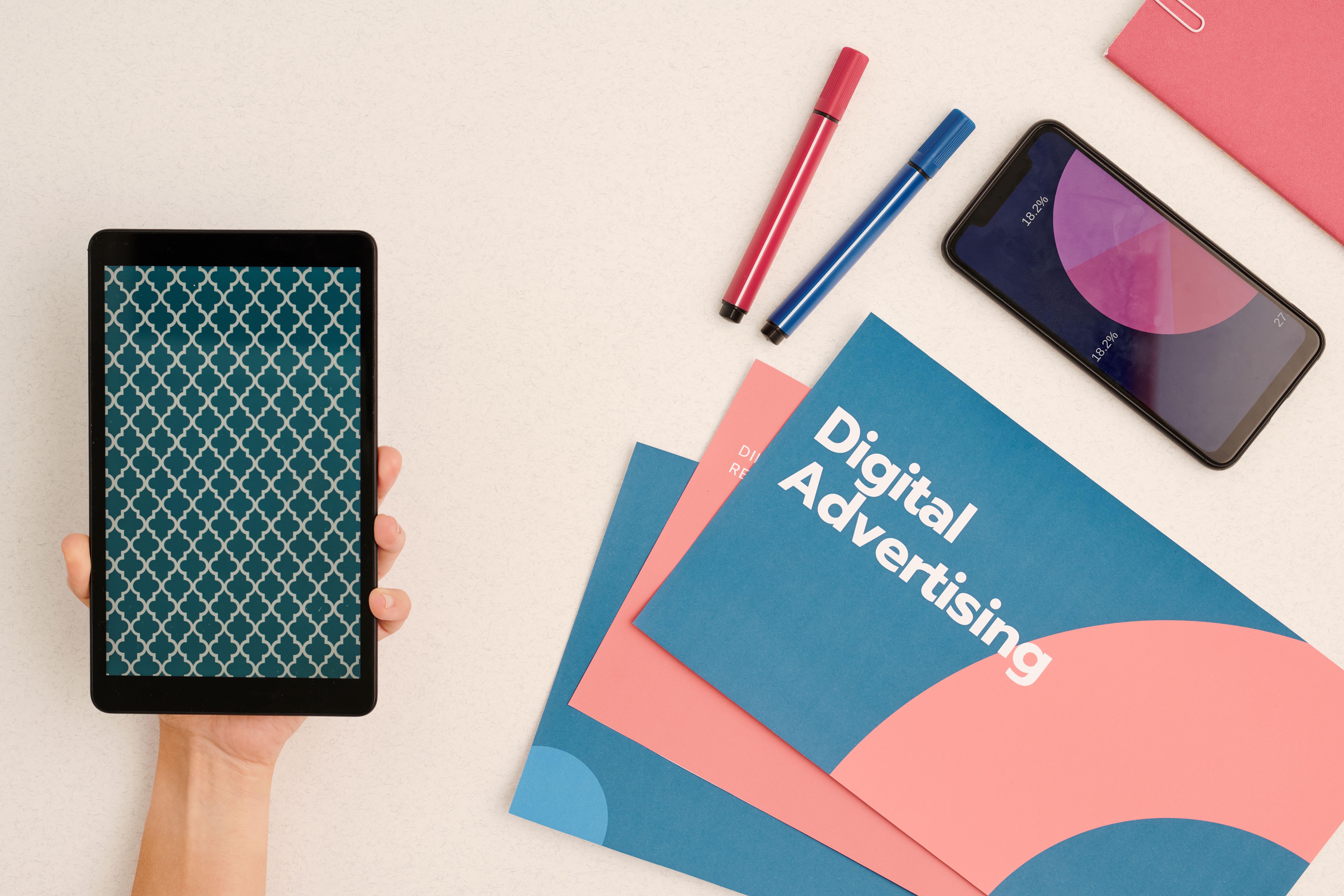 Flat lay of digital advertising materials with tablet, smartphone showing analytics, and colorful marketing brochures on a desk