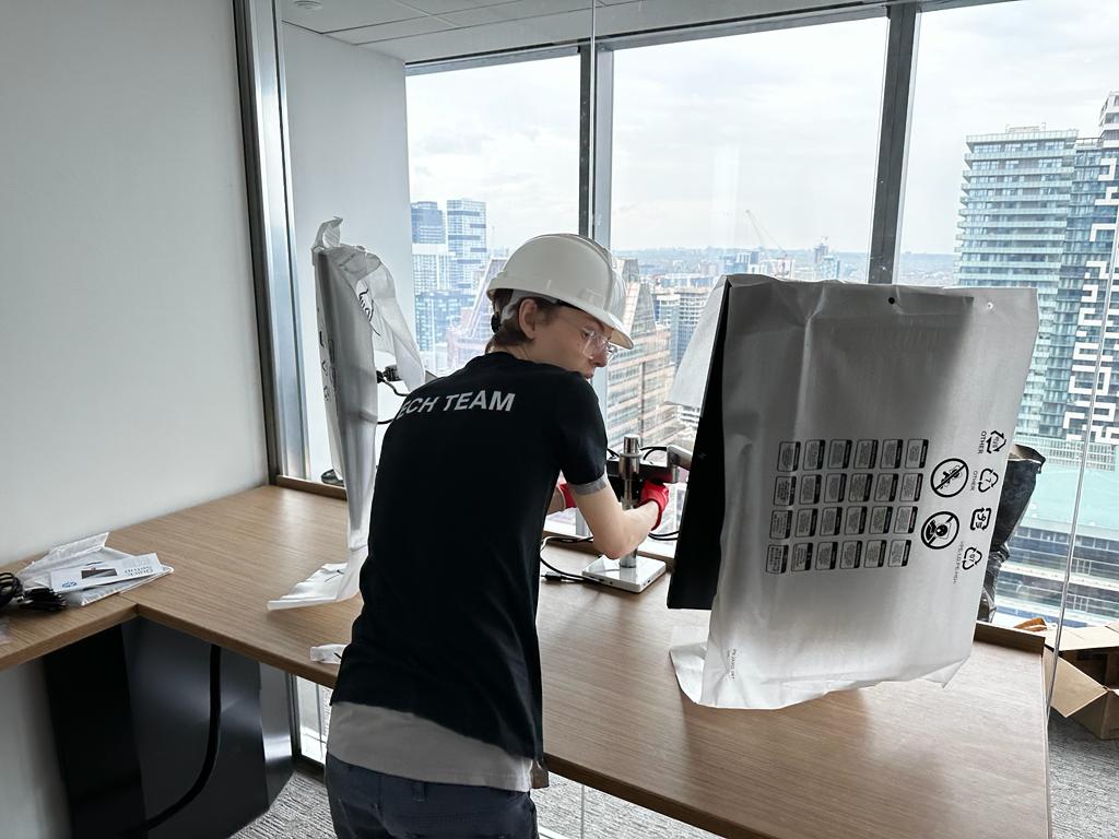 Technician disconnecting monitors and workstation equipment at office desk