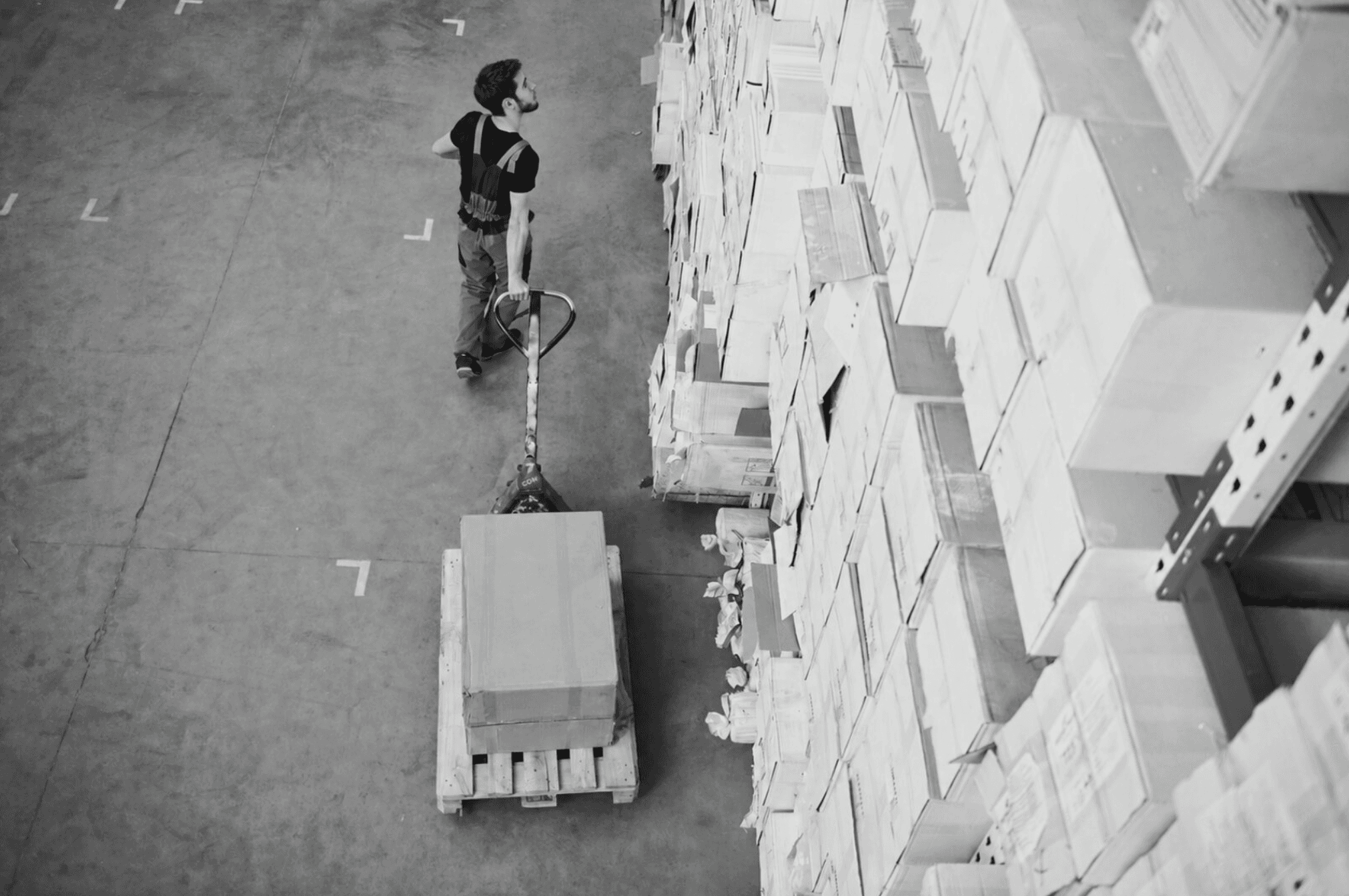 Logistikmitarbeiter transportiert eine Palette mit einem Hubwagen durch das Lager.
