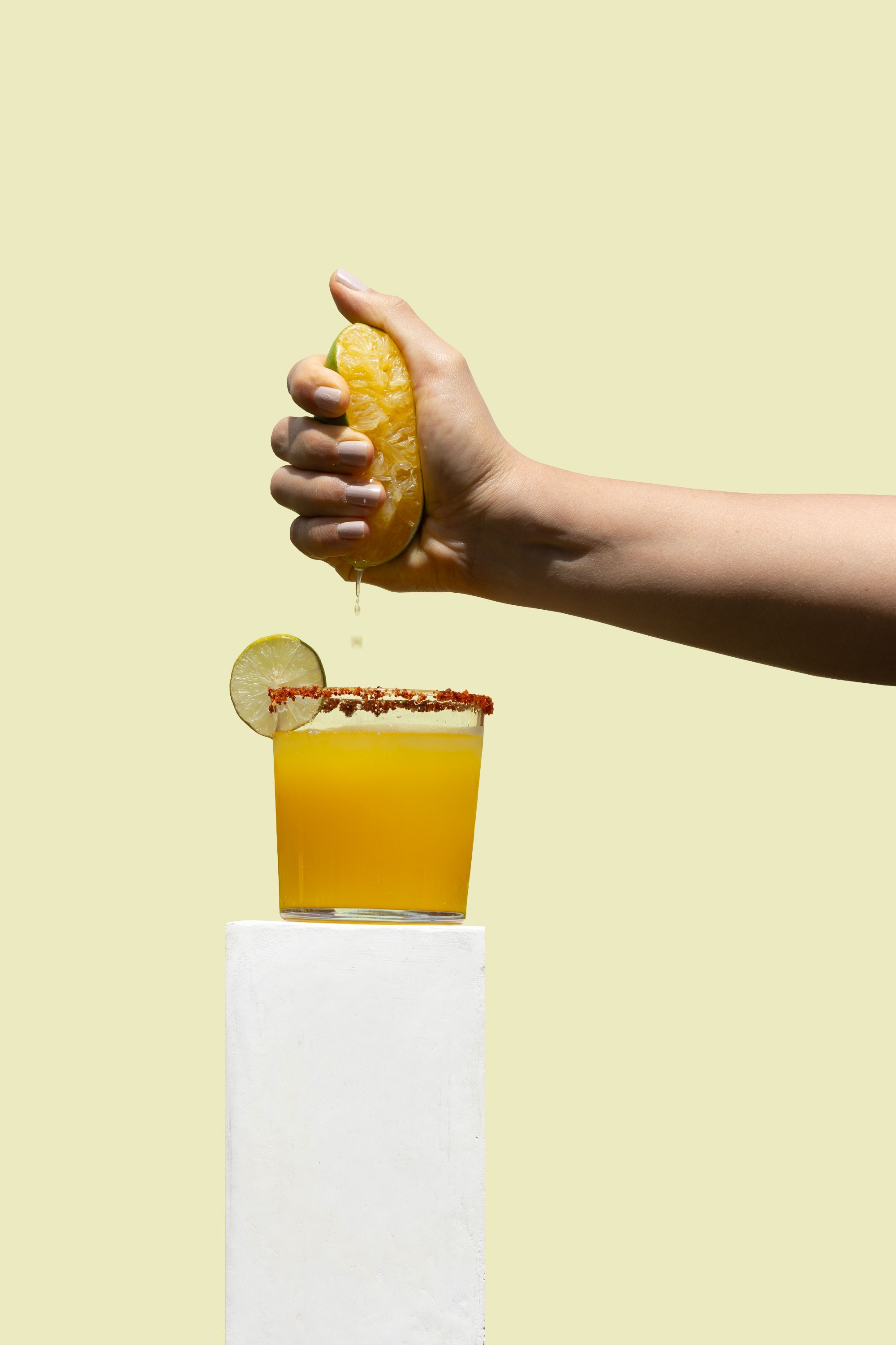 Hand squeezing a lemon over a golden mezcal Solmano cocktail in a rocks glass