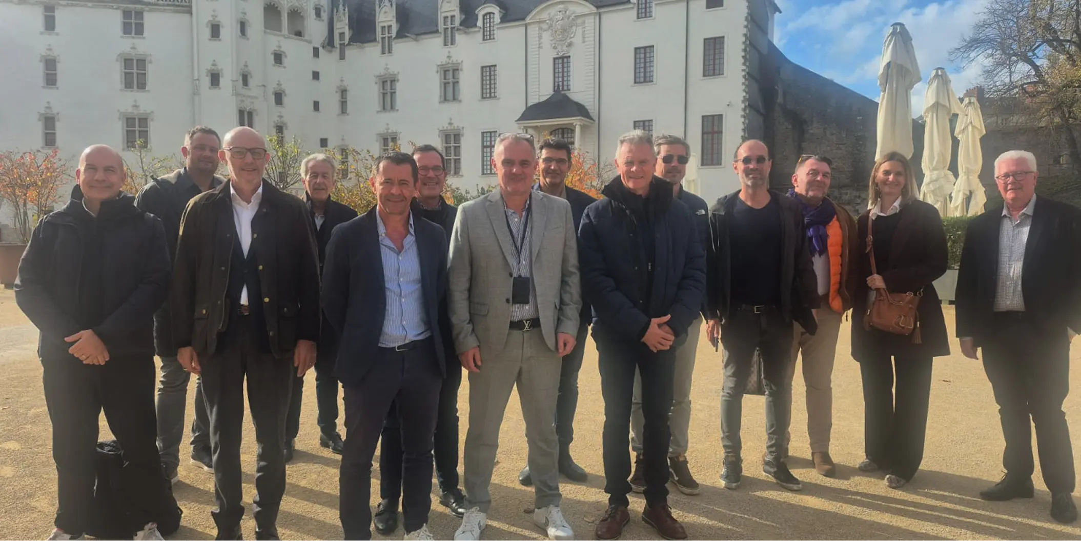 Groupe de professionnels de la transaction pharmaceutique posant devant un élégant bâtiment blanc.
