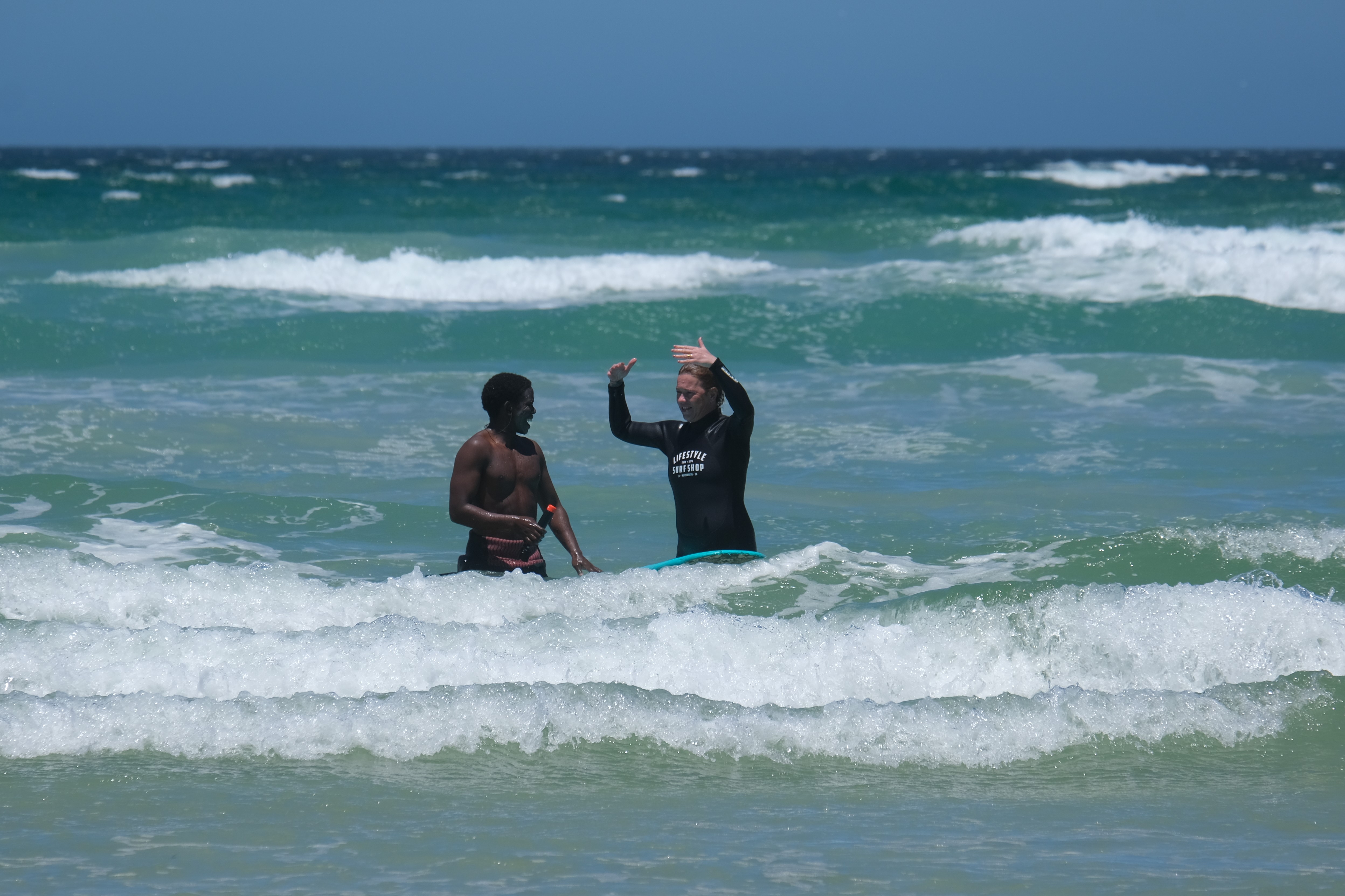 A surf coach with his student in the water talking, Muizenberg beach in Cape Town
