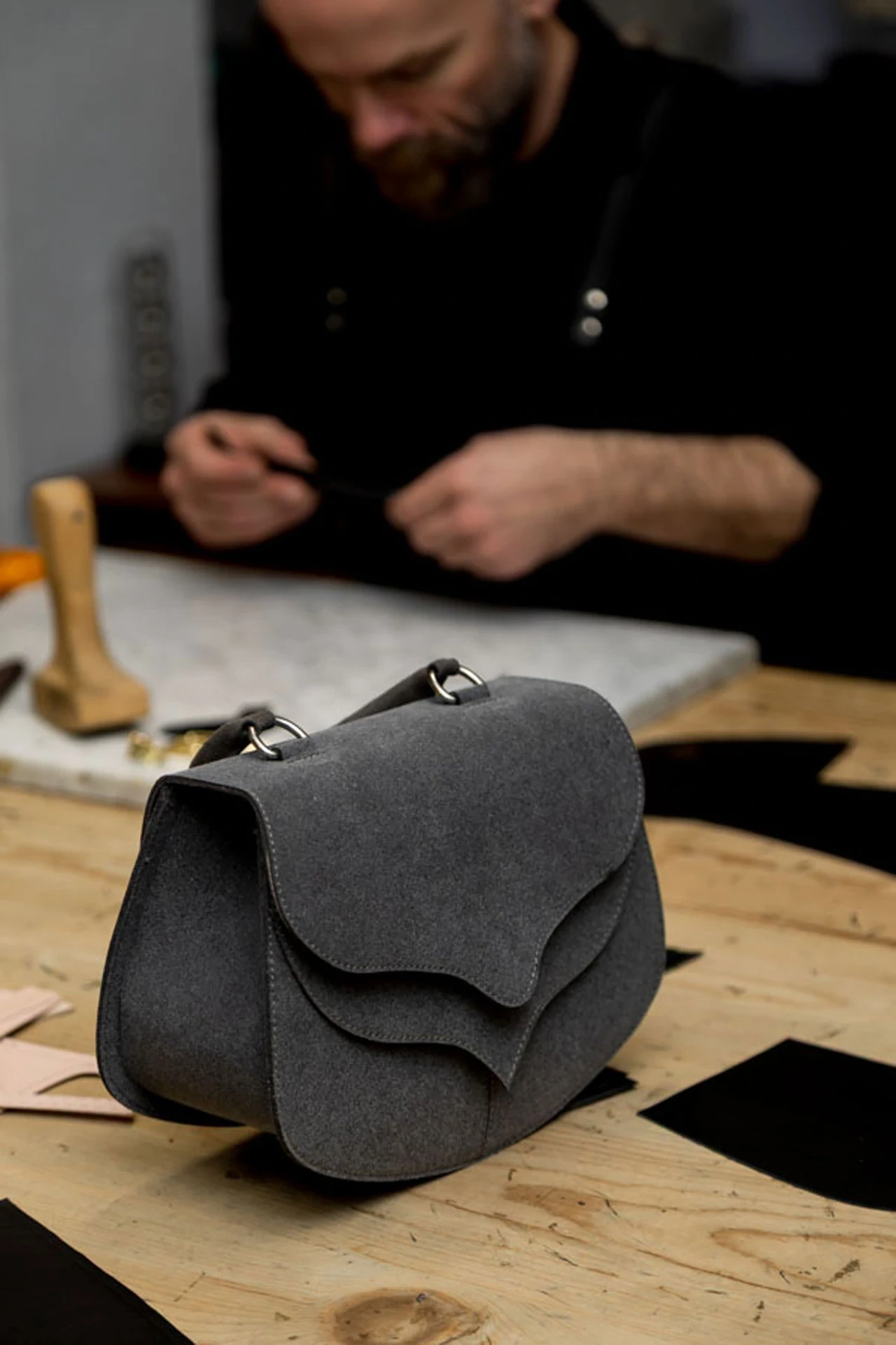 A grey handbag prototype on the workbench, with a maker working behind it.