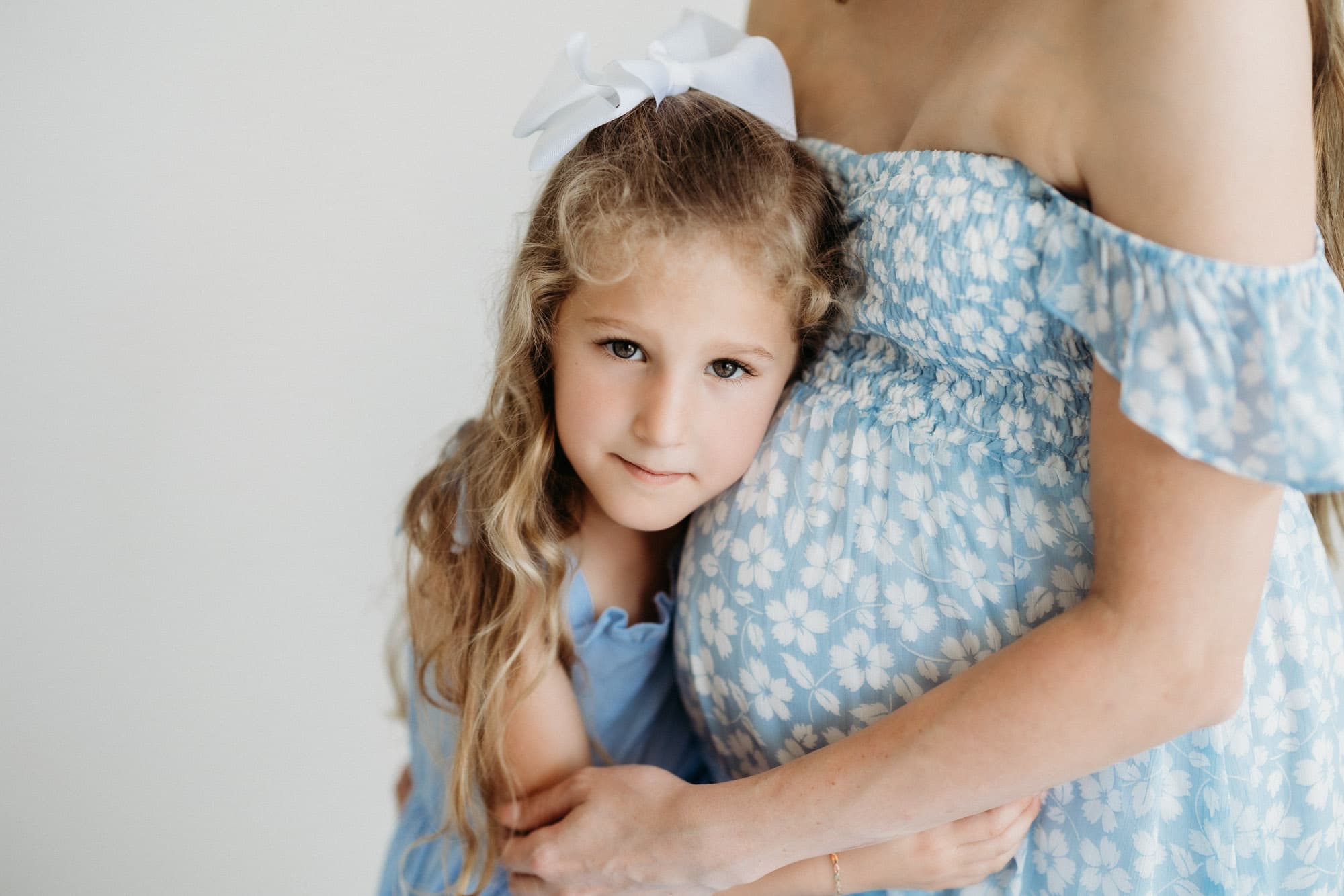 A child lovingly hugs her mother’s pregnant belly in this natural light maternity photo at Revelator Studio in Shreveport, showcasing the bond between mother and child in a photography studio.