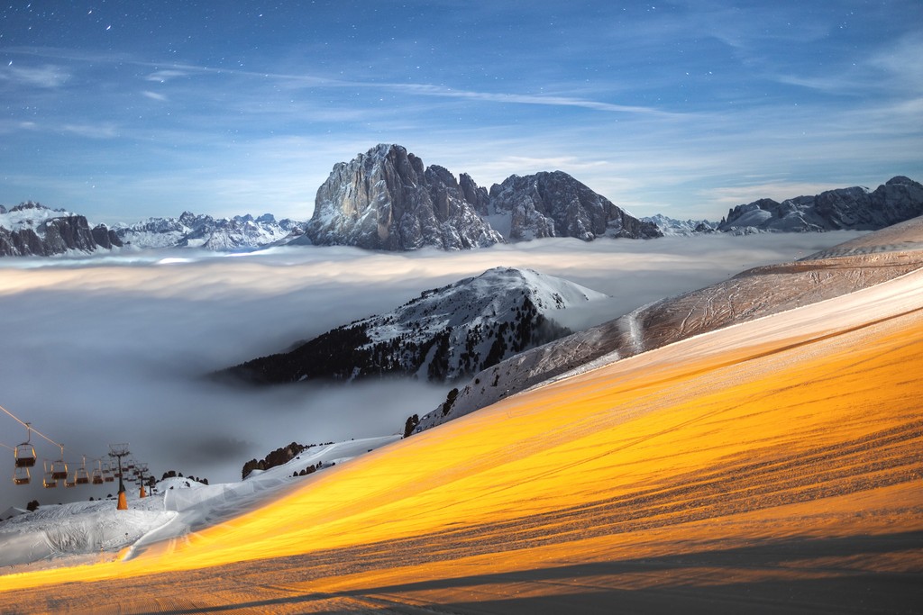 A ski slope glowing orange with rocky and snowy mountains in the background