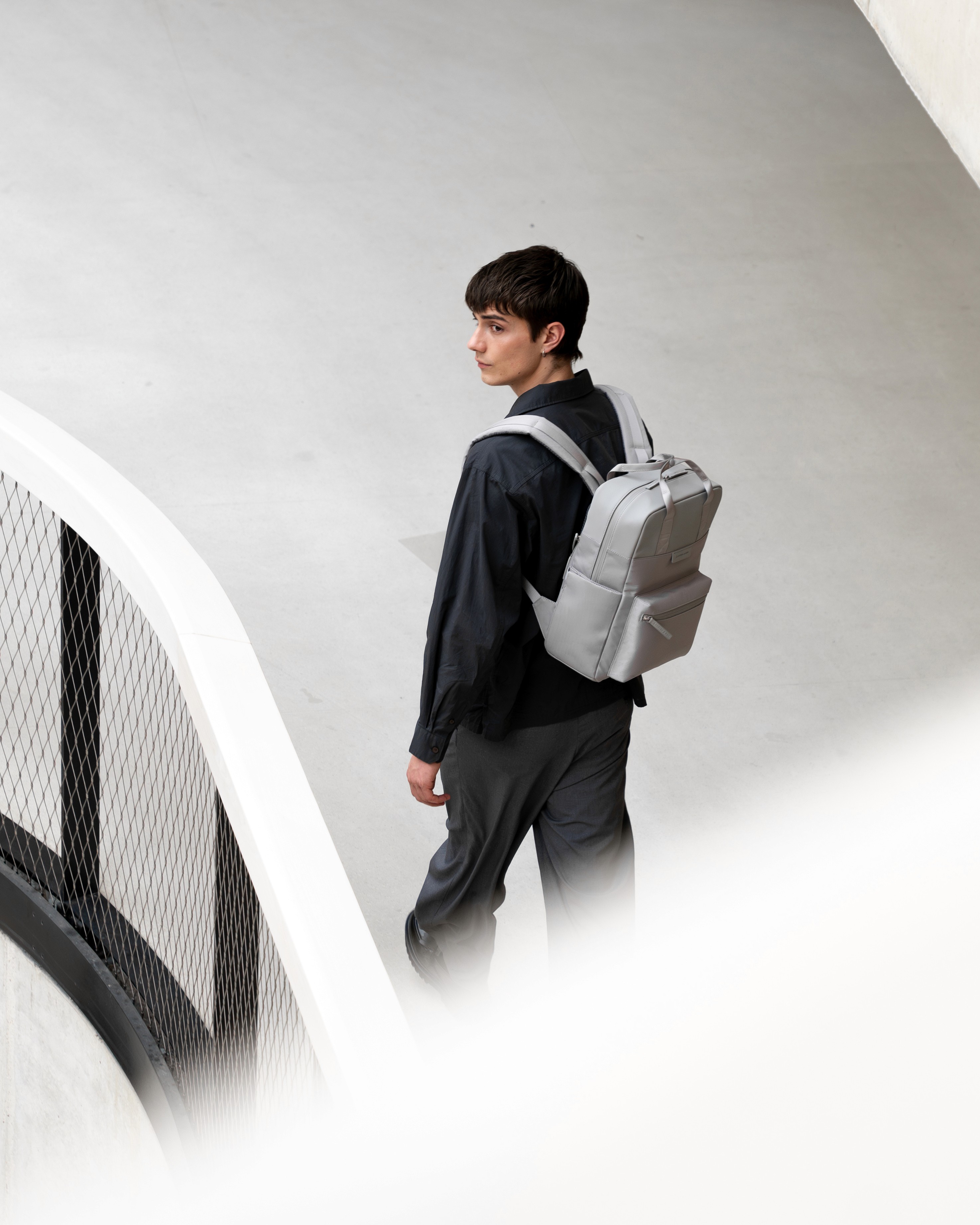 Vu de trois quarts, un homme porte un sac à dos gris clair