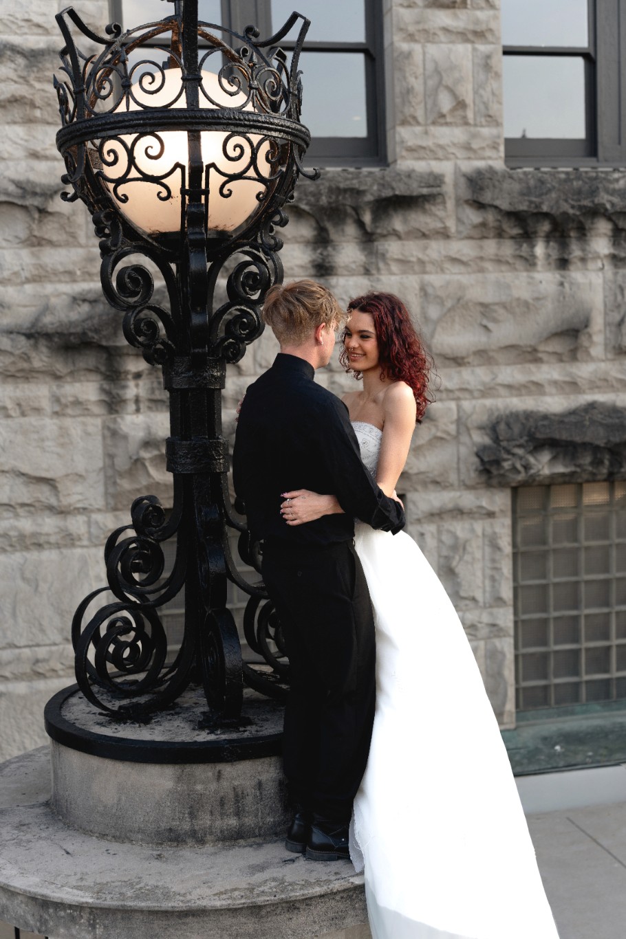 A couple joyfully celebrates in front of a rustic stone building.