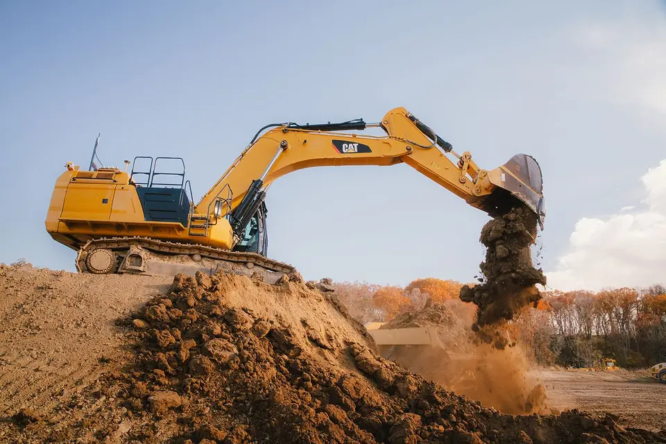 Two yellow Caterpillar excavators operating on a rocky construction site, one with a breaker attachment.