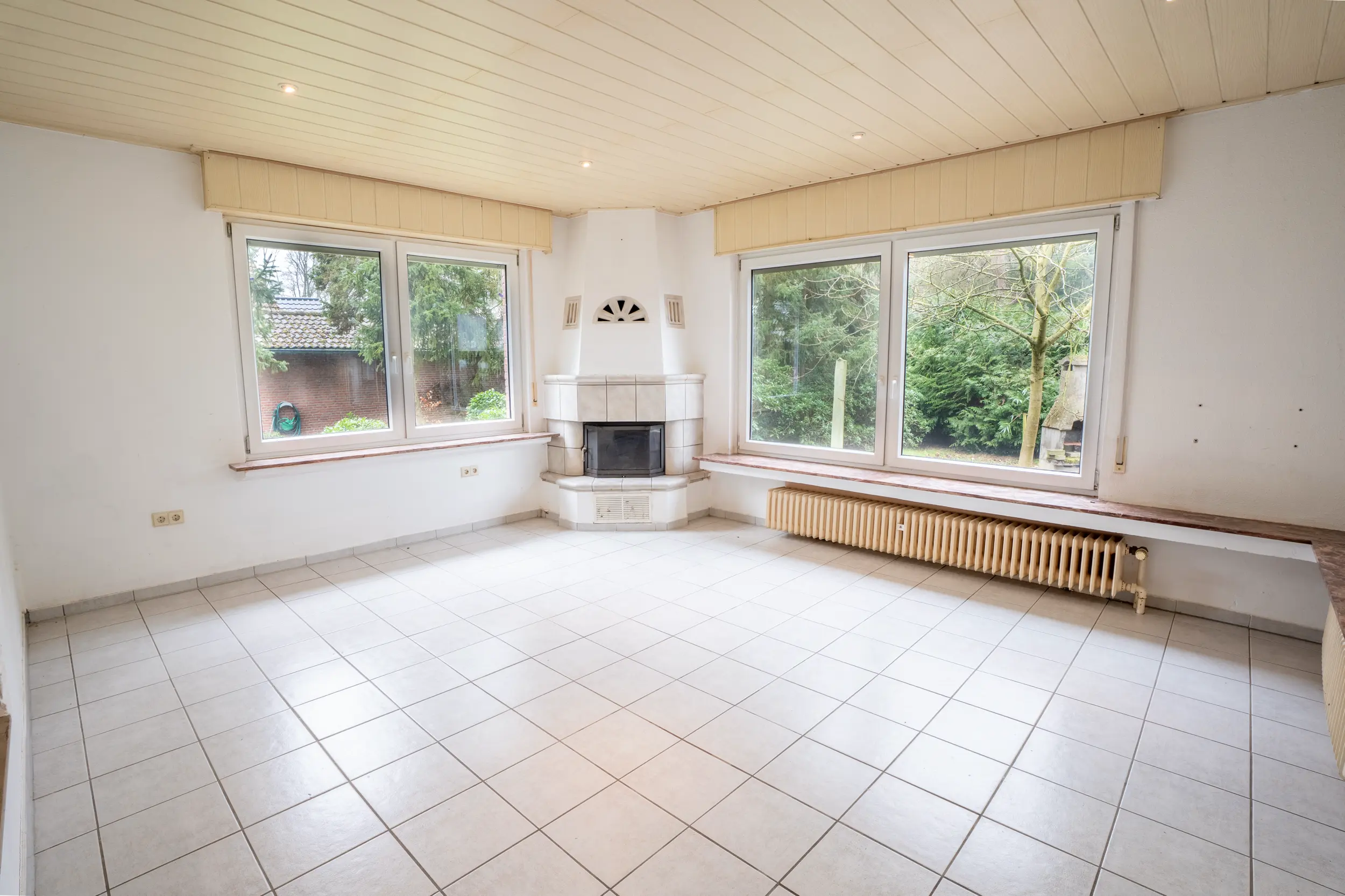 Großzügiger Wohnbereich mit großen Fenstern, Fliesenboden und Kamin in heller Raumgestaltung im Einfamilienhaus in Gronau-Epe.