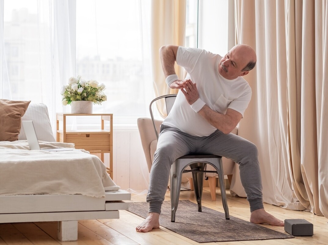older man doing a beginner seated cardio workout for weight loss in his apartment
