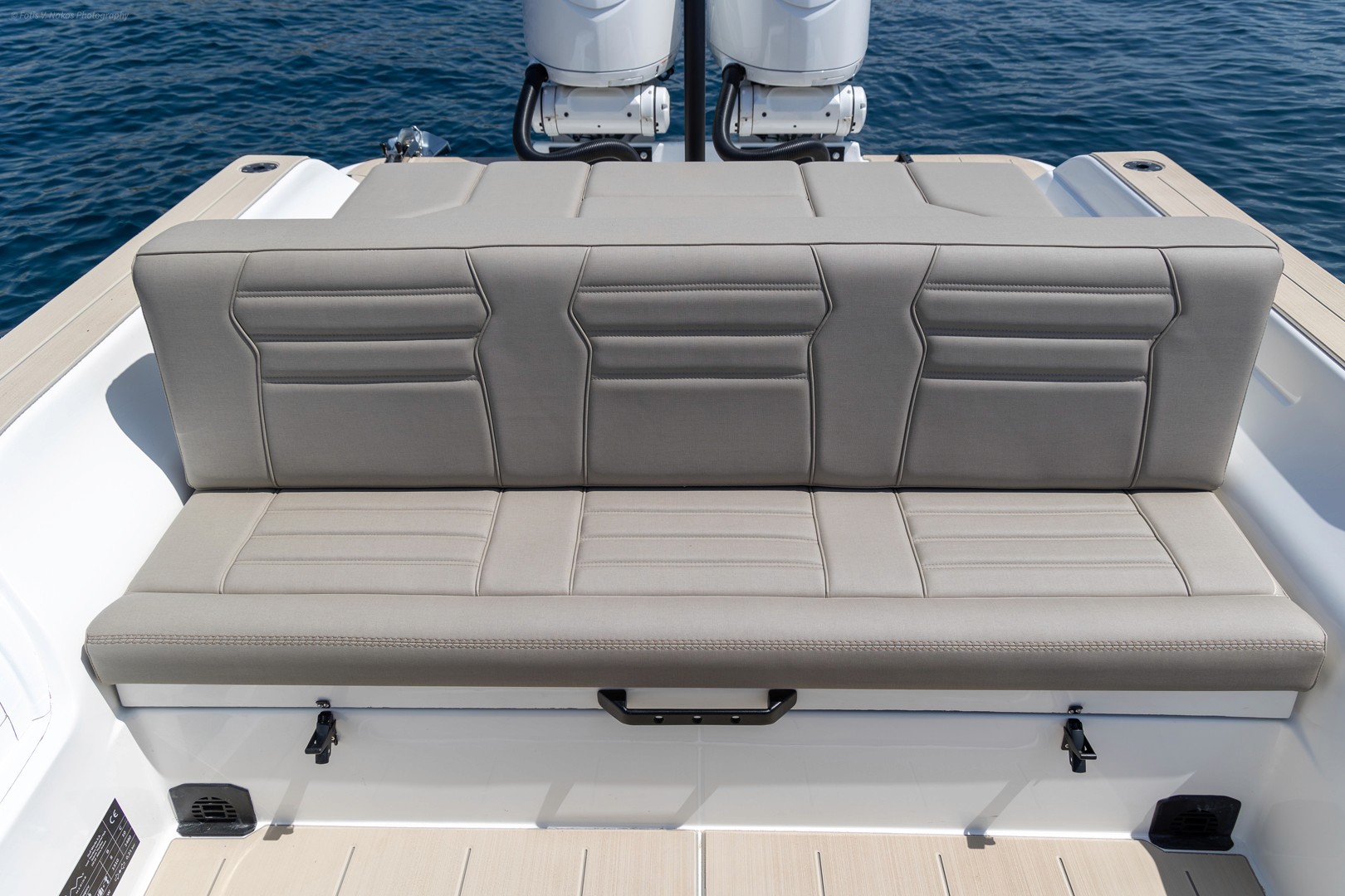 Luxury yacht stern seating area with gray leather upholstery and twin outboard motors overlooking calm blue waters.