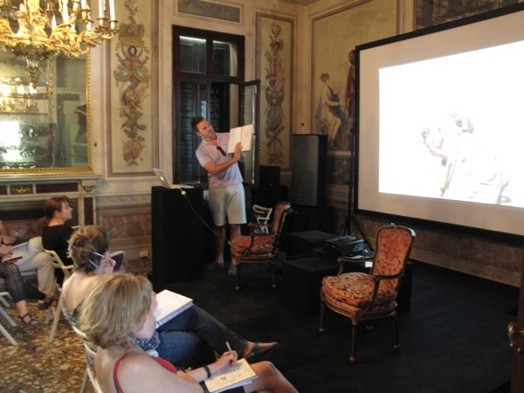 a man presents to a group of people something from a book with the help of an image projection on the wall